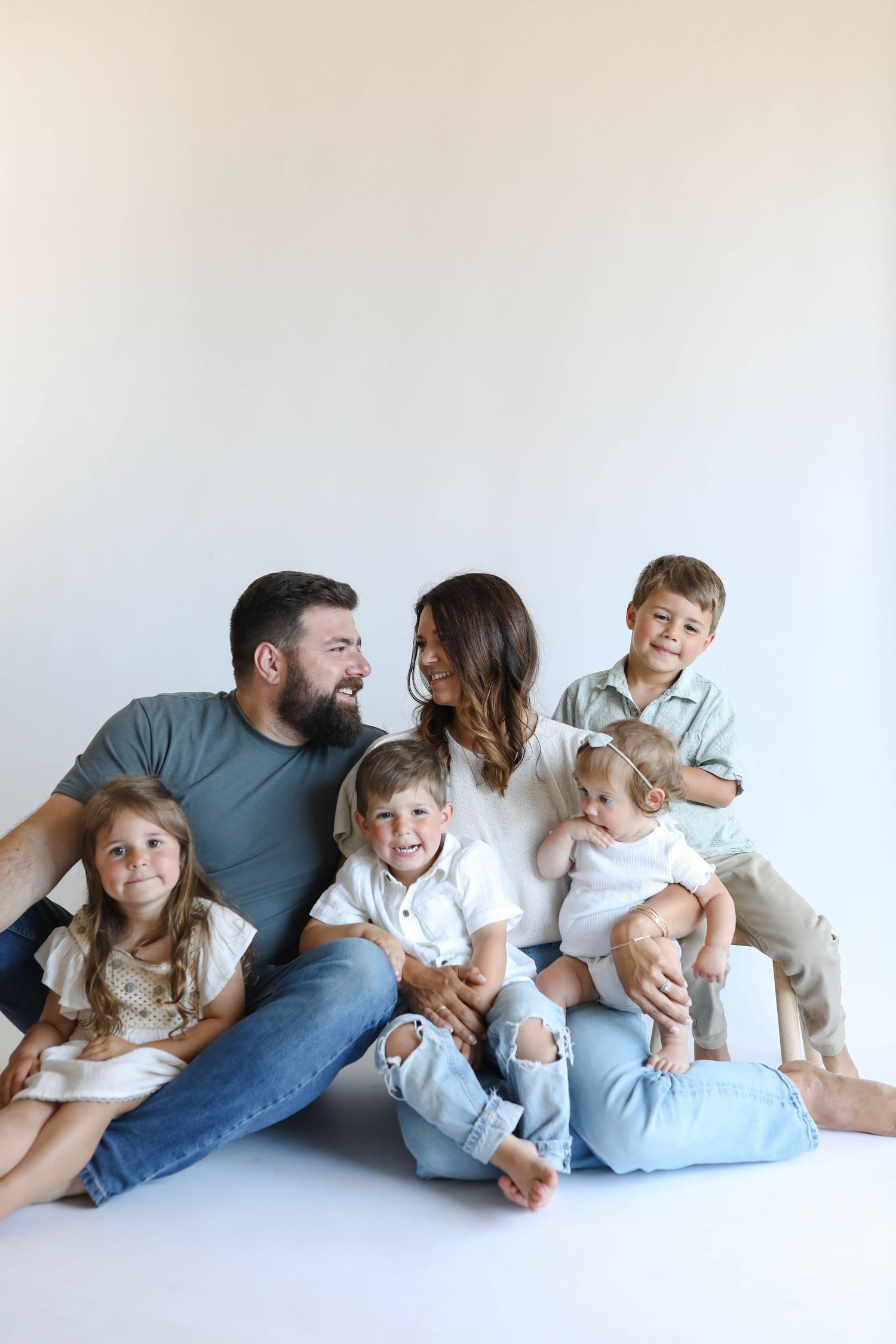 A happy family of six poses together against a white background, with parents and four young children smiling.
