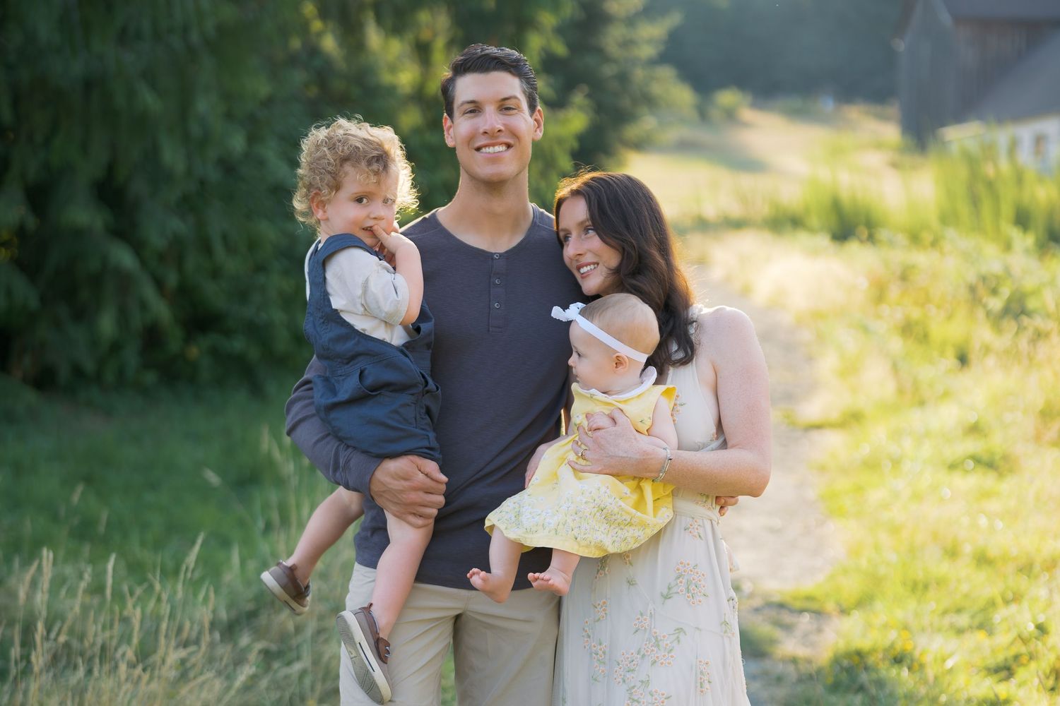 Happy young family with two small children posing outdoors in a sunny green field during a family portrait session.