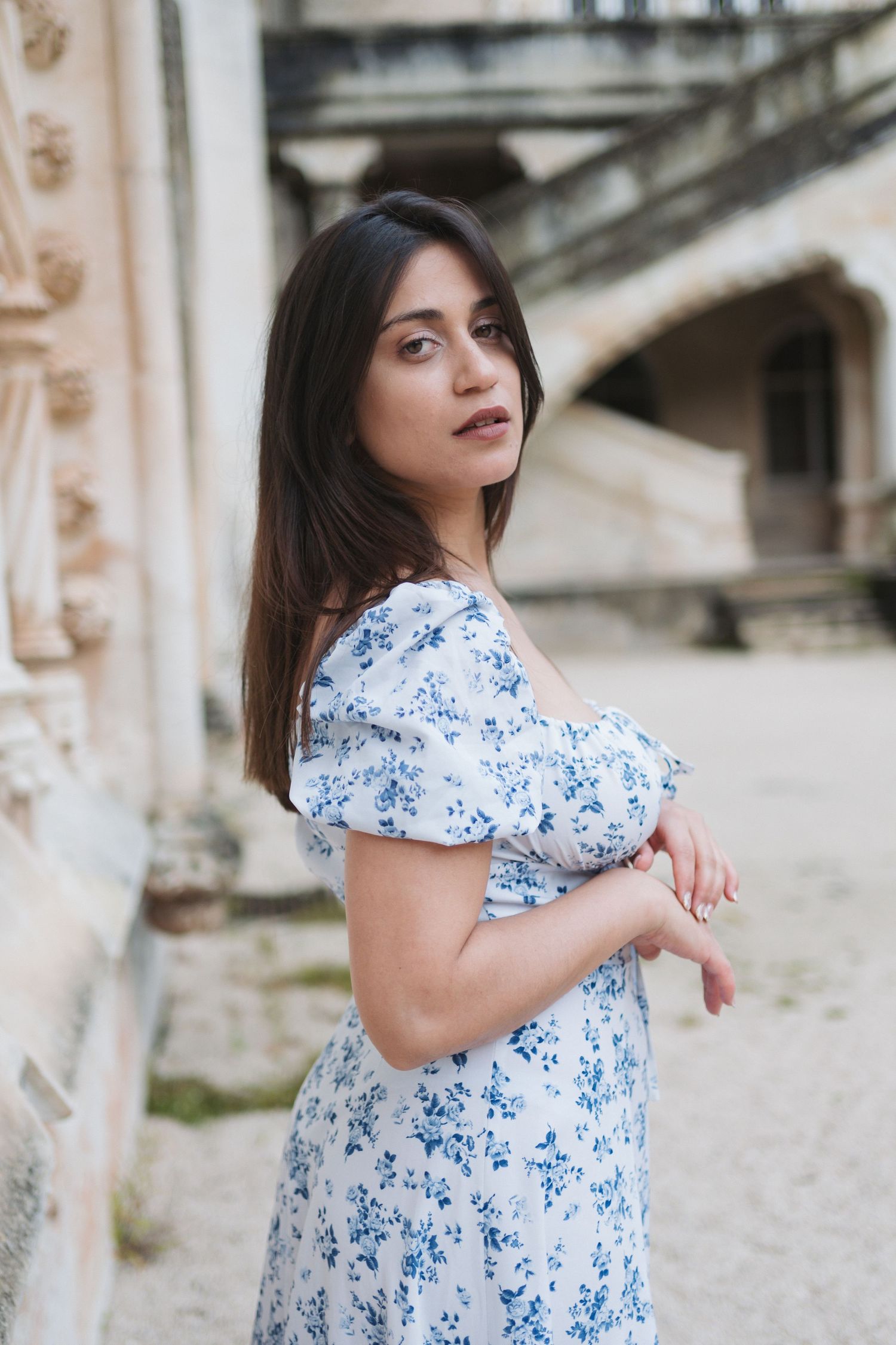Woman in blue floral dress poses against vintage architecture.
