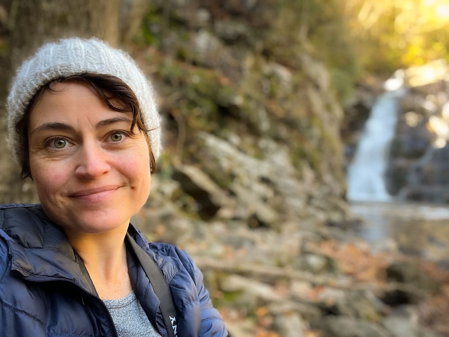 Portrait of the photographer on a hike wearing a knit hat with a waterfall in the background