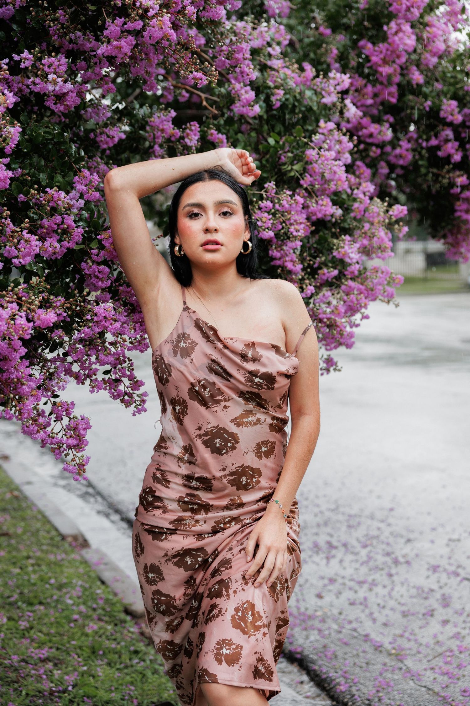 A figure poses gracefully in a brown patterned dress against a backdrop of vibrant purple bougainvillea flowers.