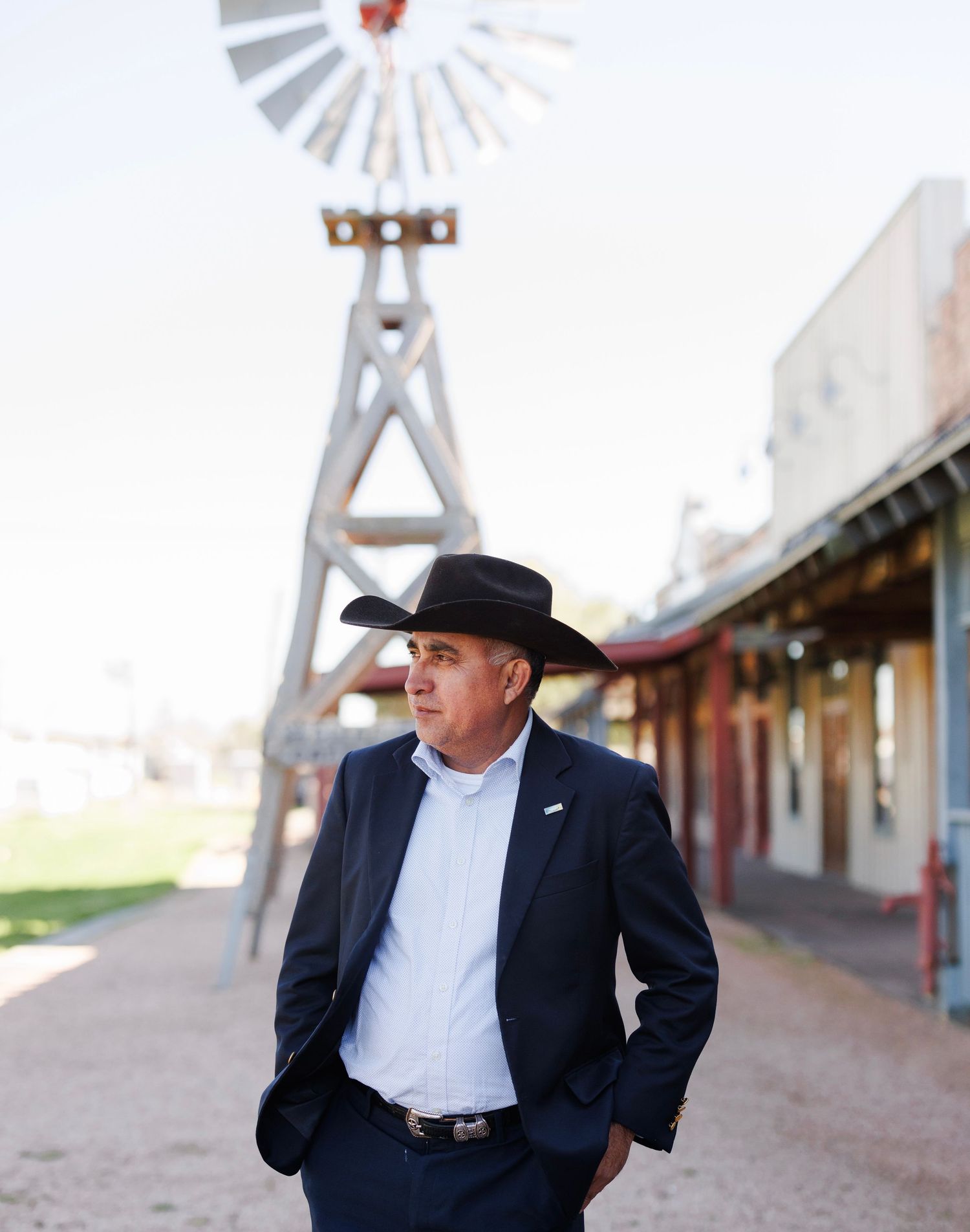 Person in western wear stands contemplatively near vintage windmill structure.