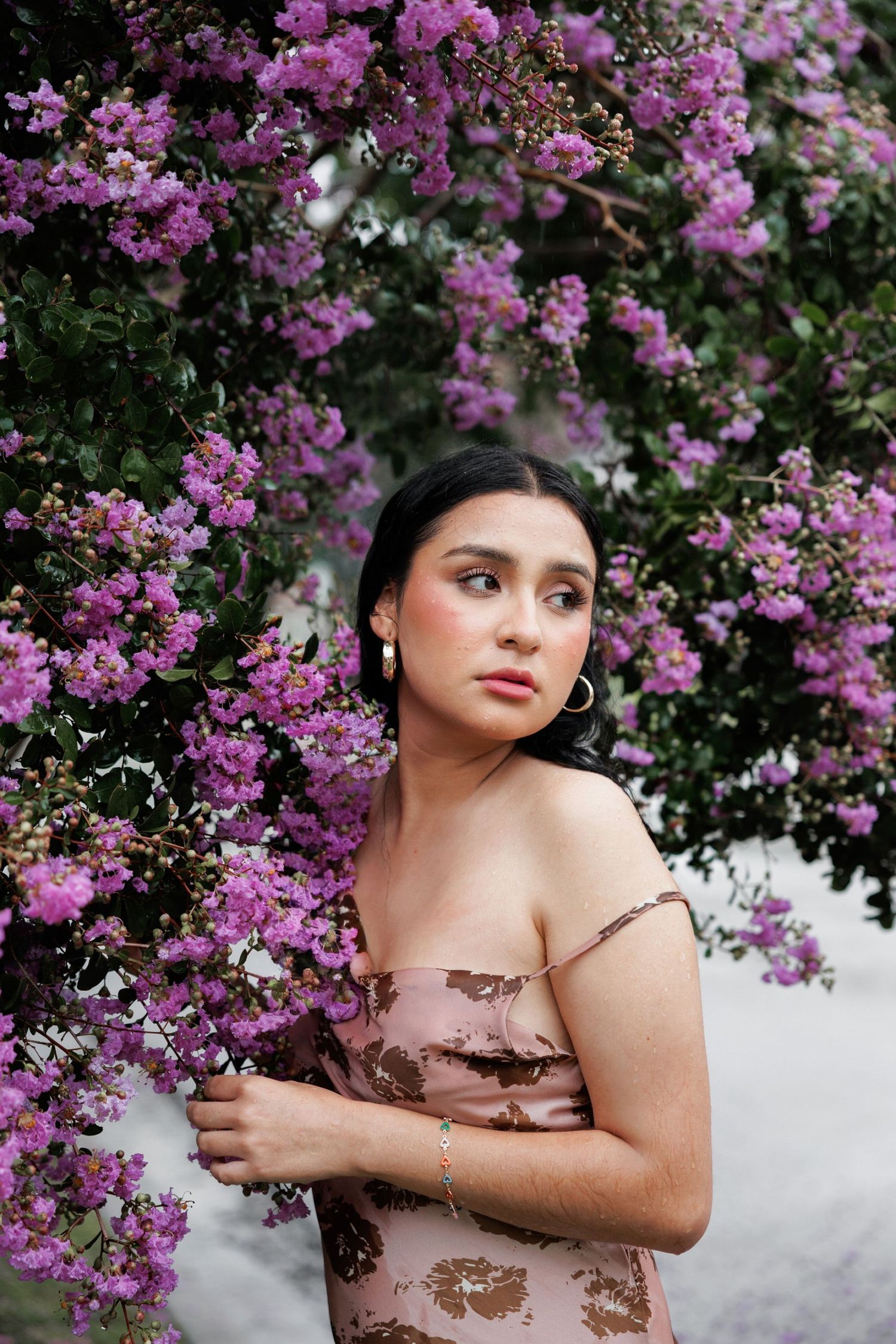 Elegant portrait surrounded by vibrant purple blossoms wearing a nude-colored dress with gold accents.