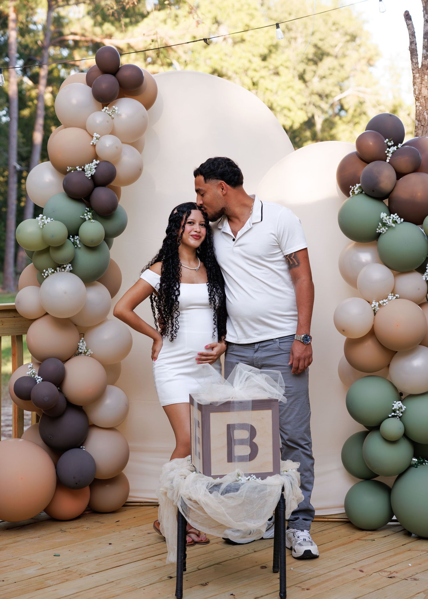 Couple poses together against elegant balloon arch display in neutral sage green and beige tones for romantic photoshoot.