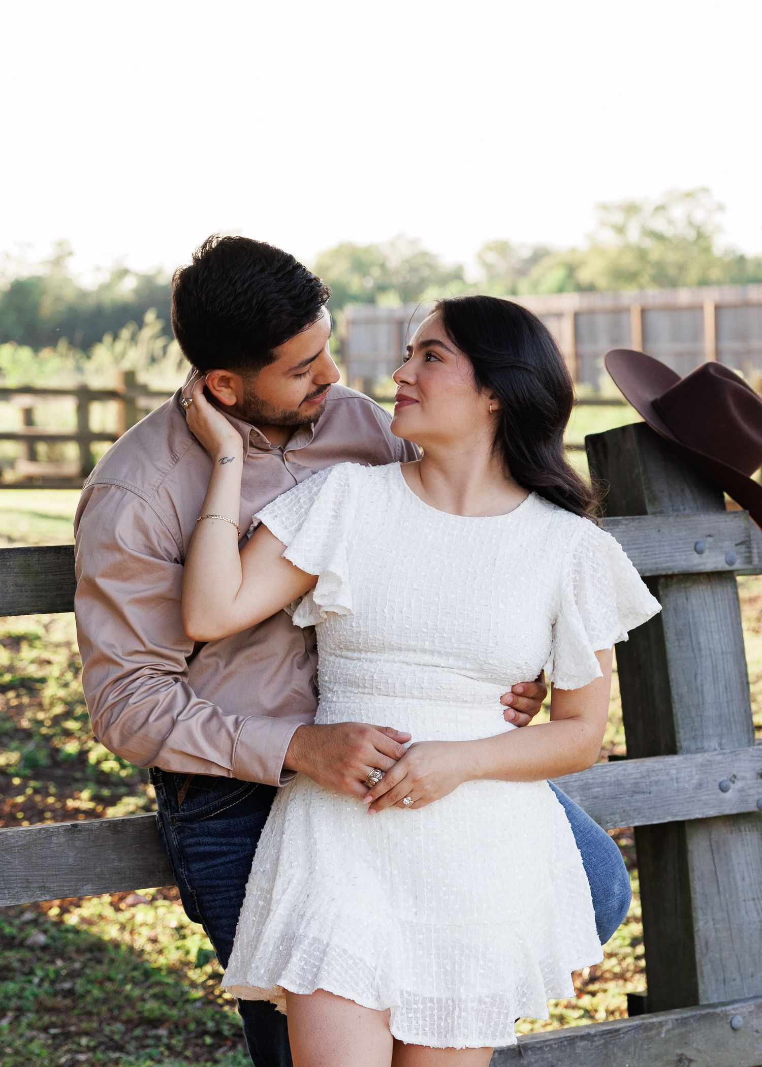 A couple shares intimate moments together during a romantic outdoor photoshoot by a wooden fence at sunset.