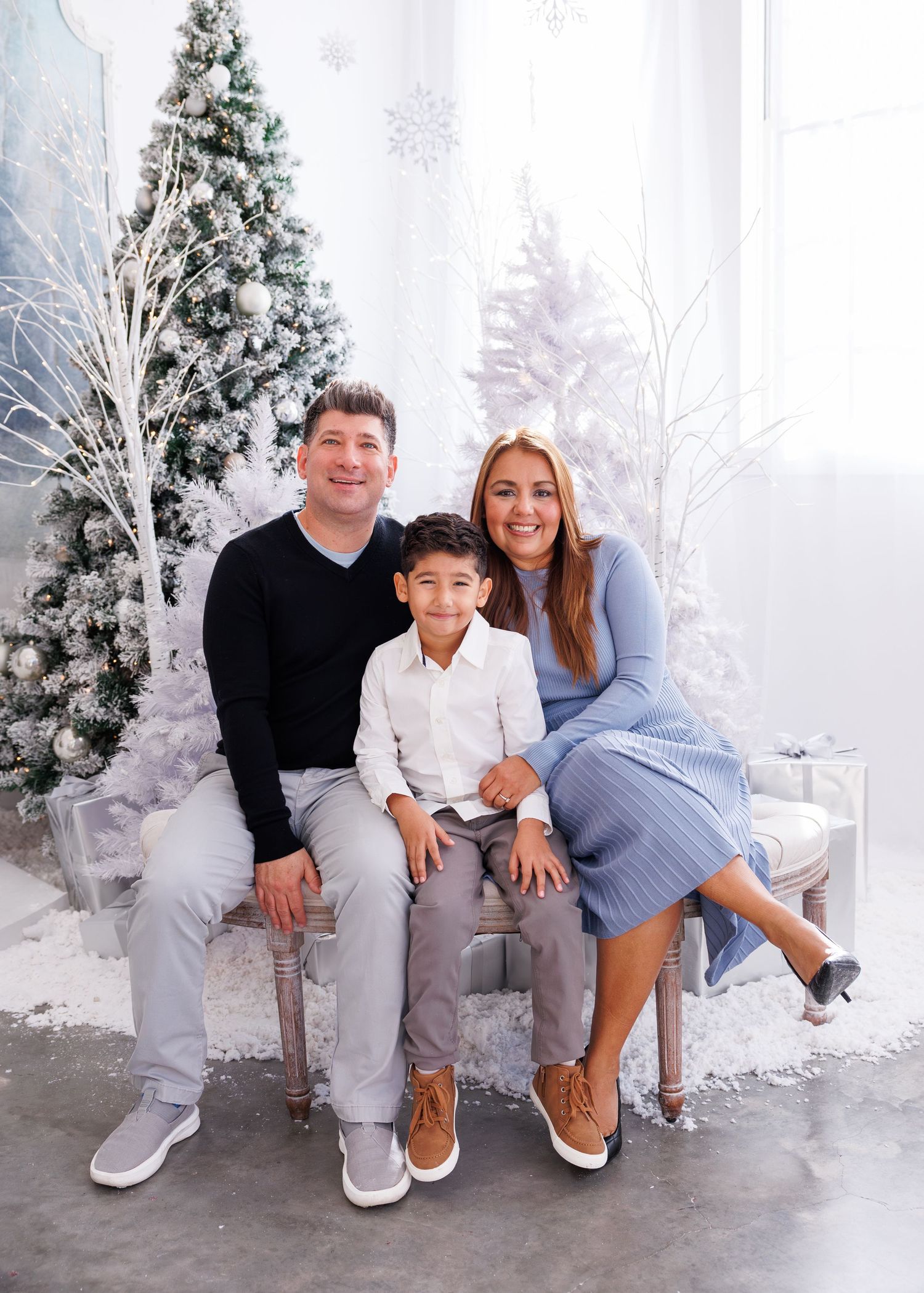 A family poses together in a winter wonderland setting with snow-covered trees and white decor for holiday photos.