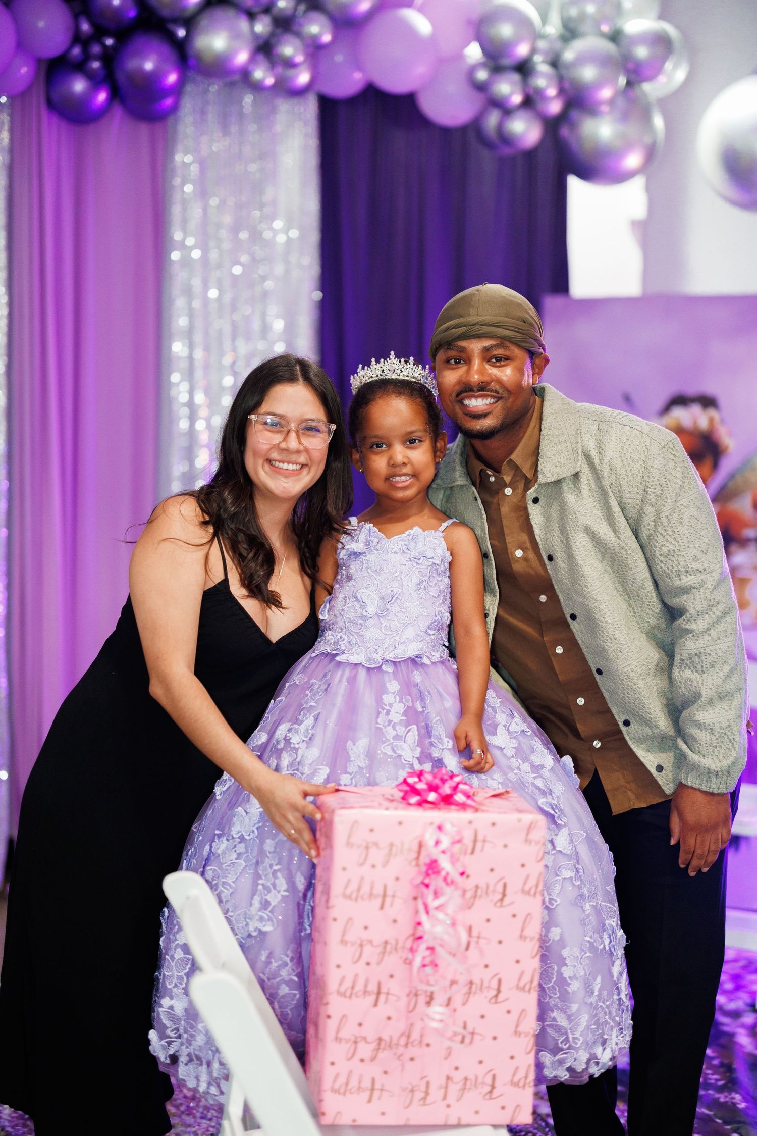 A birthday celebration with purple and silver balloons, featuring a pink cake and party guests in formal attire.