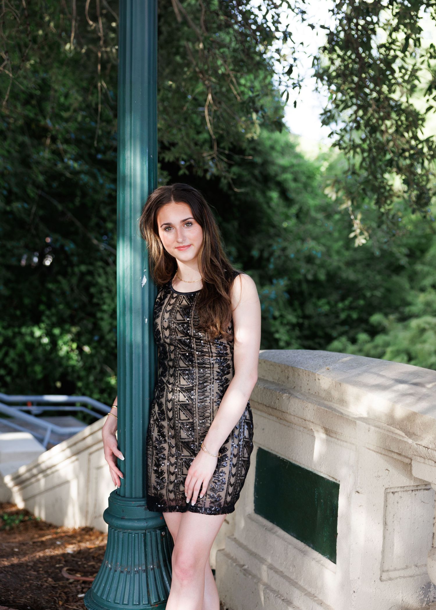 A figure wearing a lace dress poses along a stone railing in a garden setting.