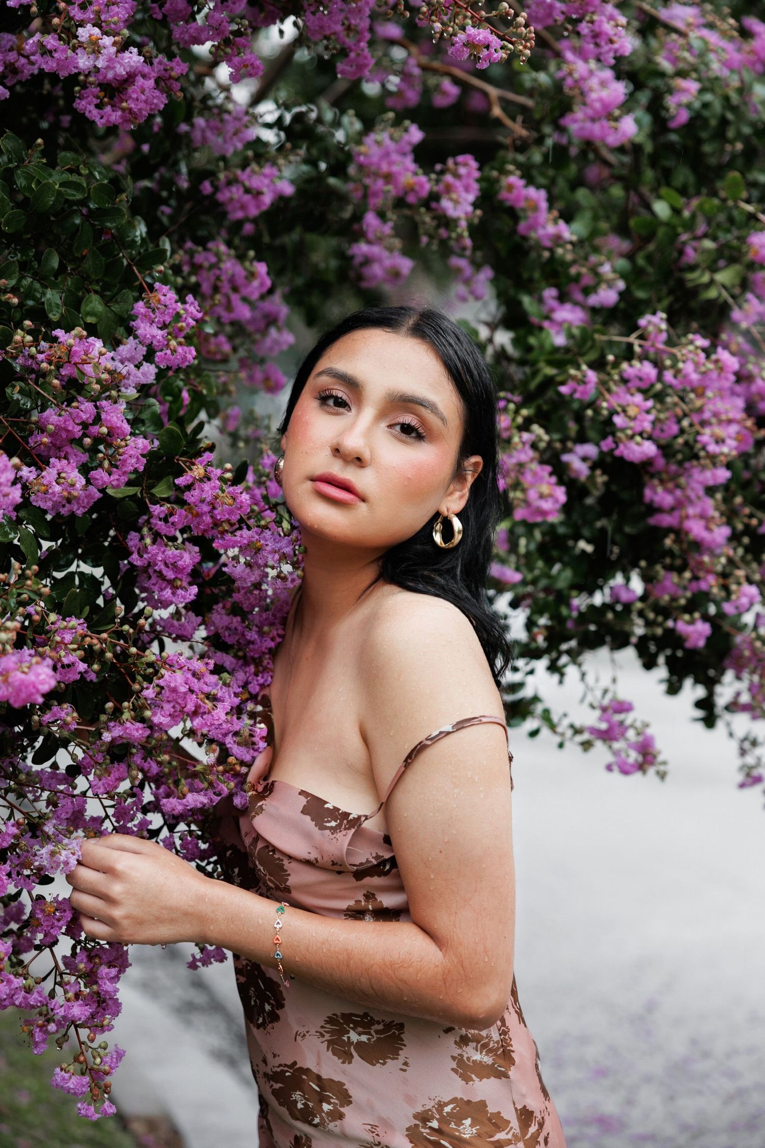 Artistic portrait against blooming purple flowers wearing a floral dress and gold hoop earrings.
