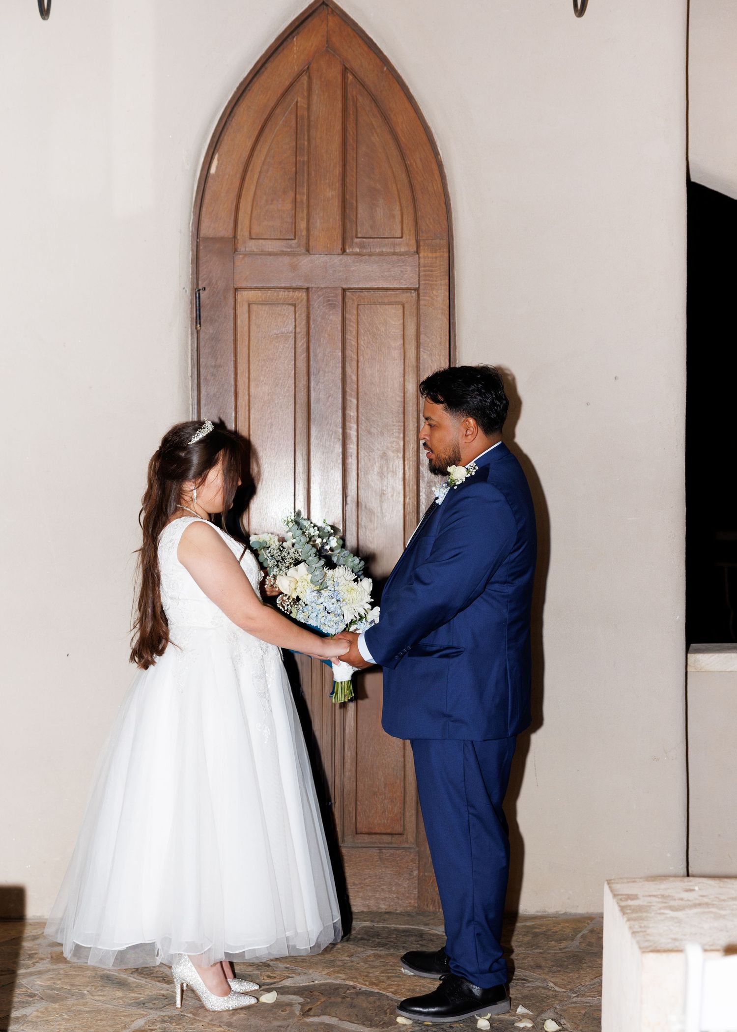 A couple shares a romantic dance moment during their wedding ceremony in front of an elegant wooden church door.