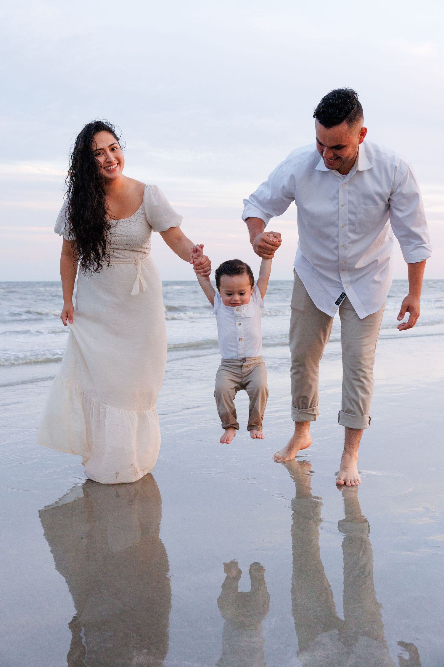 Family in white outfits playing together on a reflective beach at sunset.