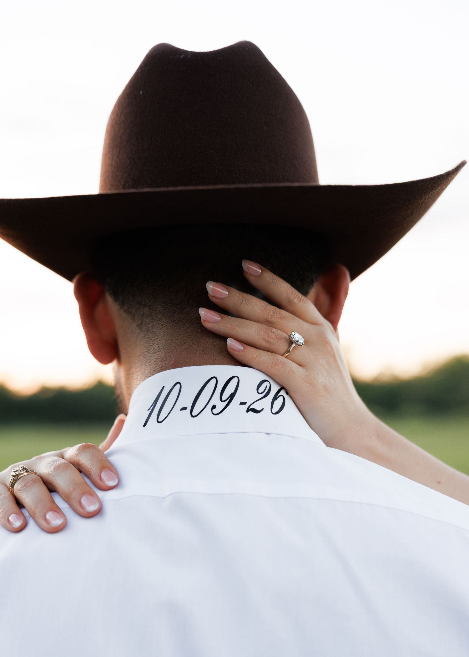 Close-up view of embroidered wedding date on white dress shirt collar with hands holding black hat.