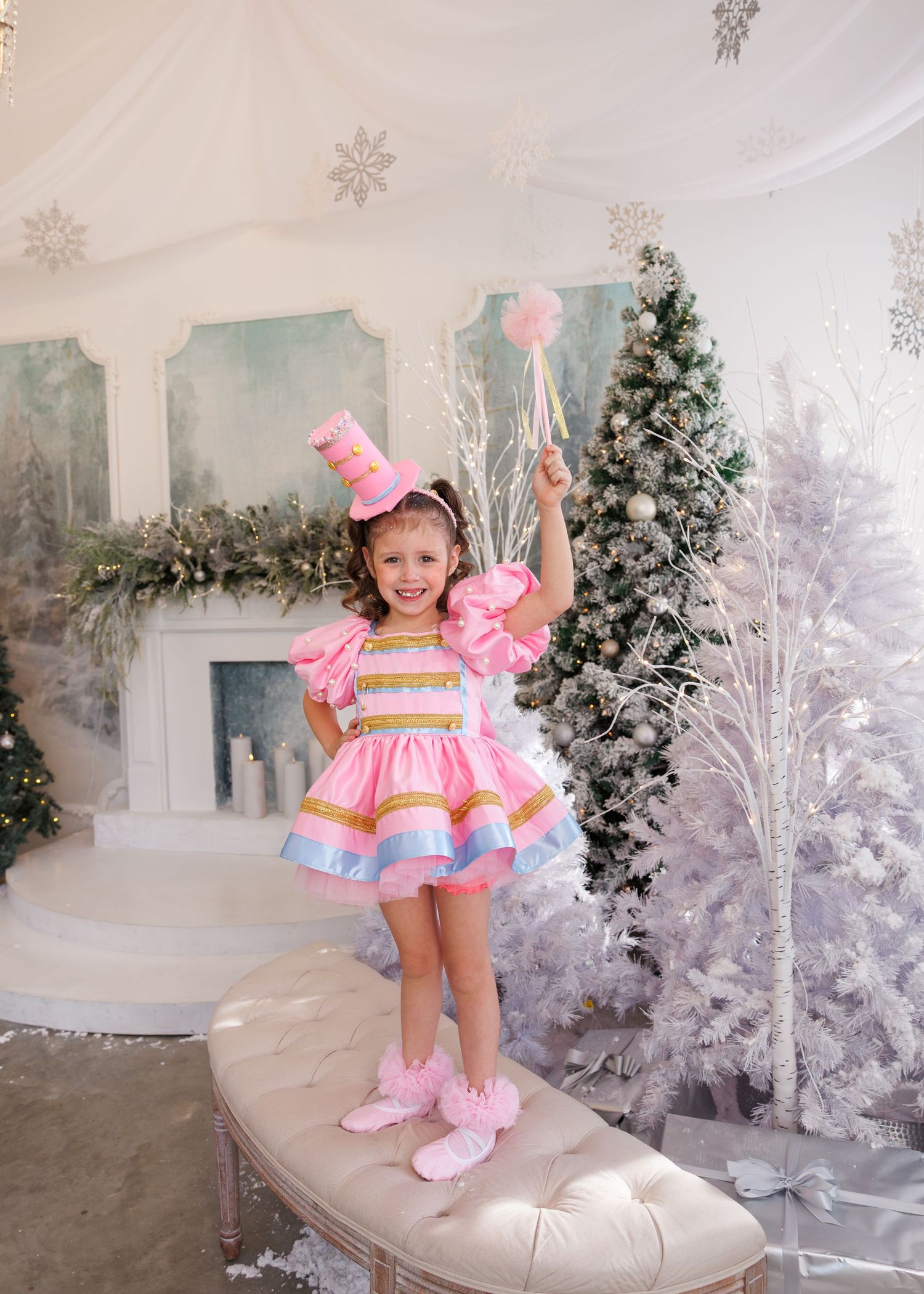A child in a pink and white dress twirls and poses in a winter wonderland setting with white trees and decorations.