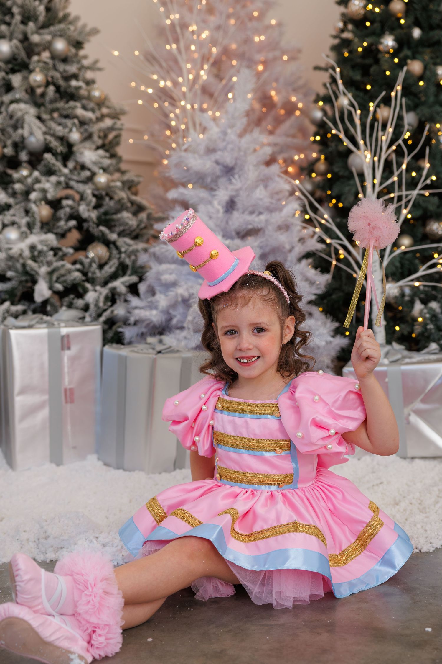 Pink and pastel dress with tiny top hat in magical Christmas scene with snowy white trees and twinkling lights.