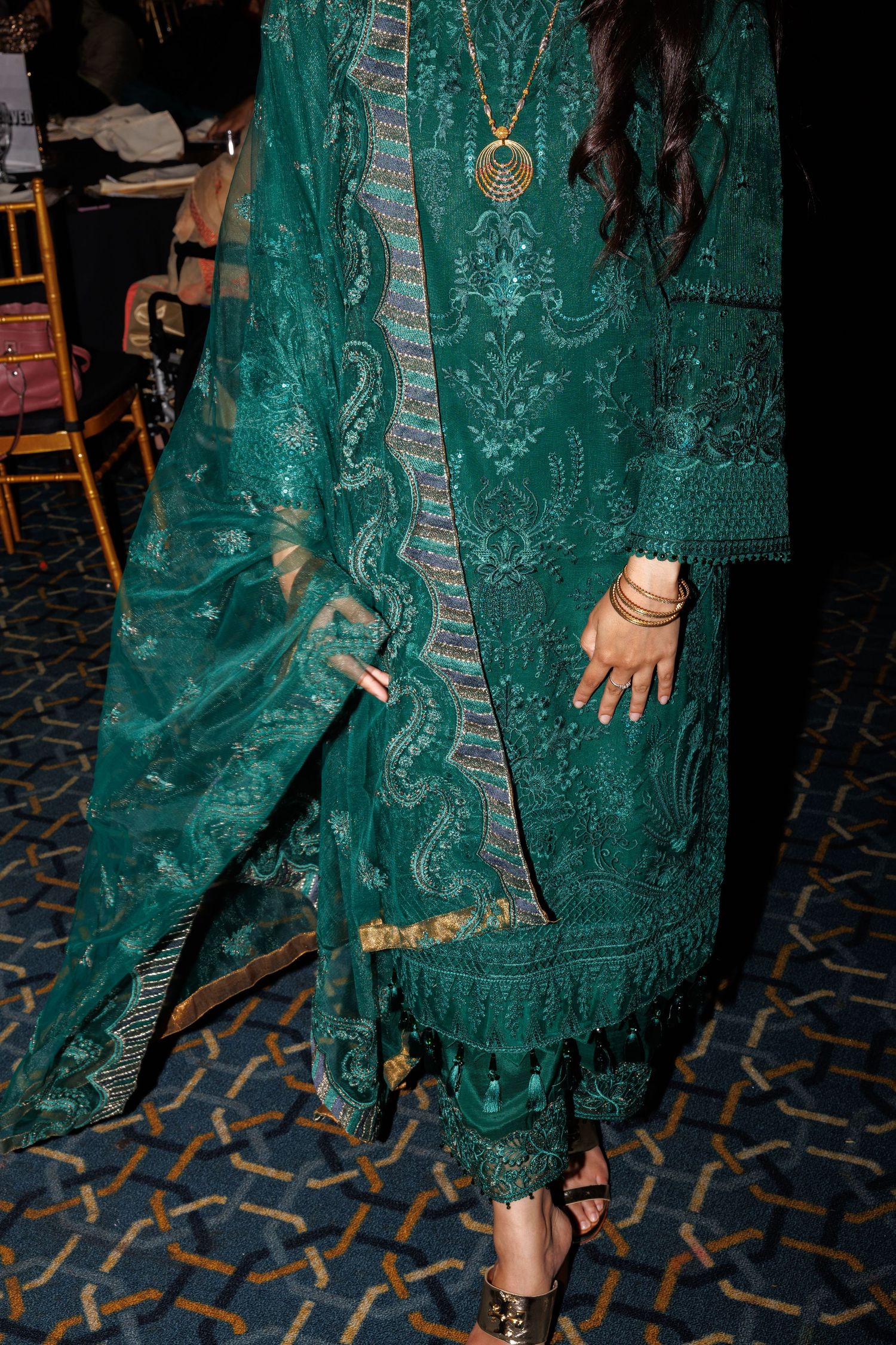Detailed view of an ornate emerald green embroidered traditional outfit with matching pants and gold jewelry.