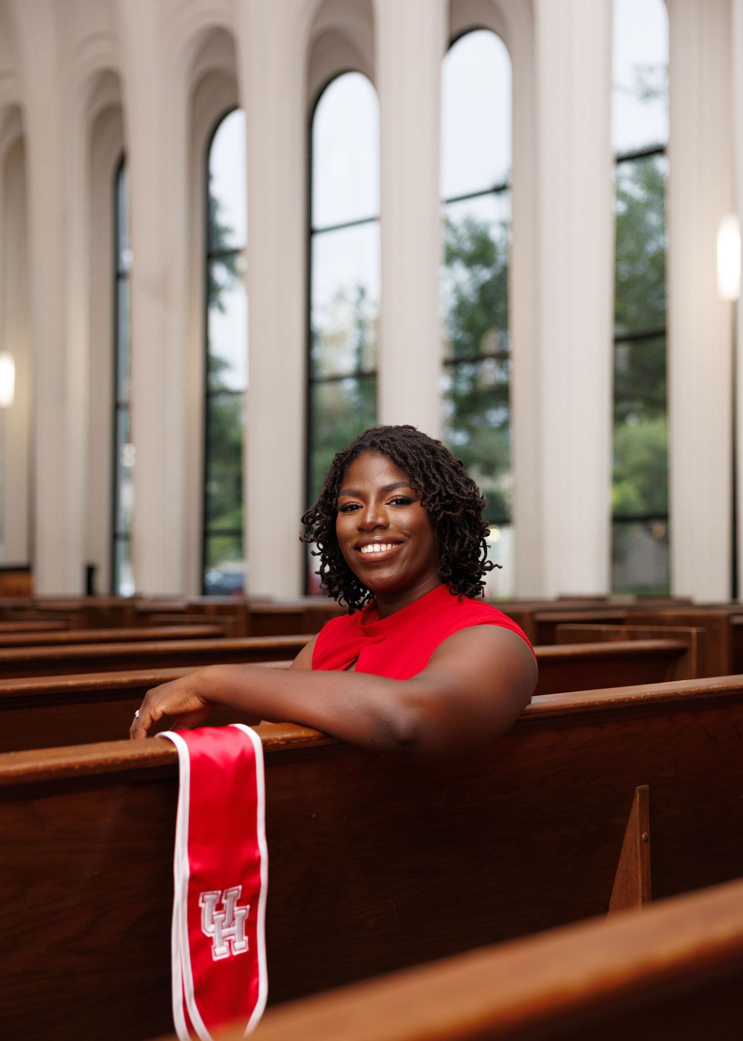 A person in a red sleeveless top sits in a wooden church pew, surrounded by tall arched windows and warm lighting.