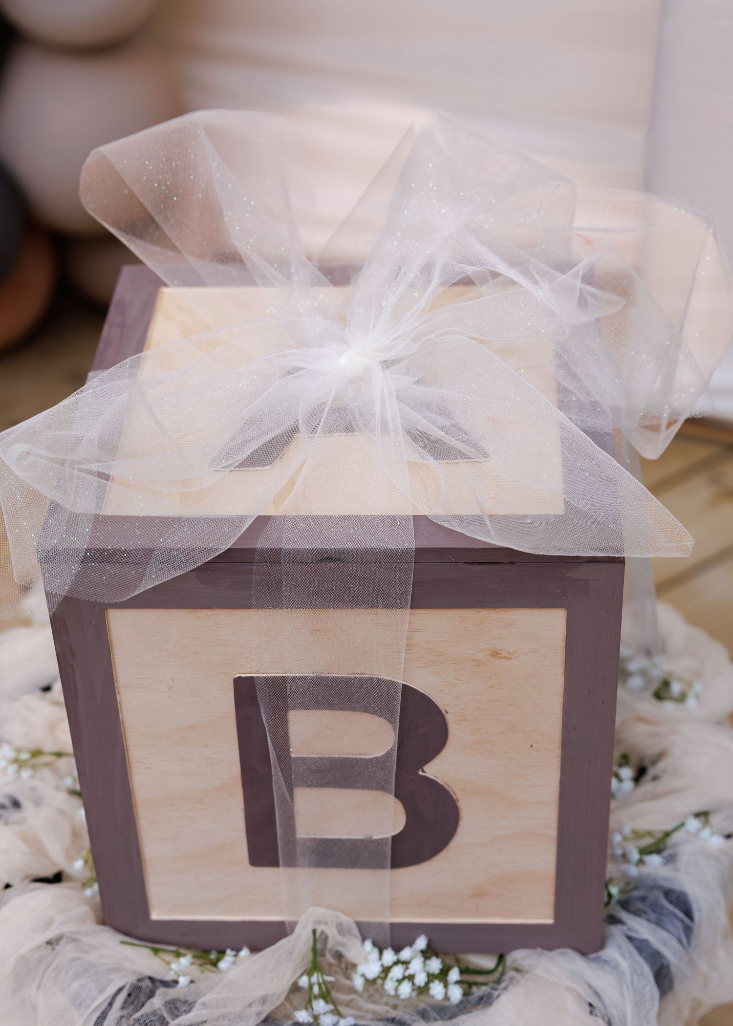 Decorative wooden box with letter B monogram topped with white tulle and baby's breath flowers.