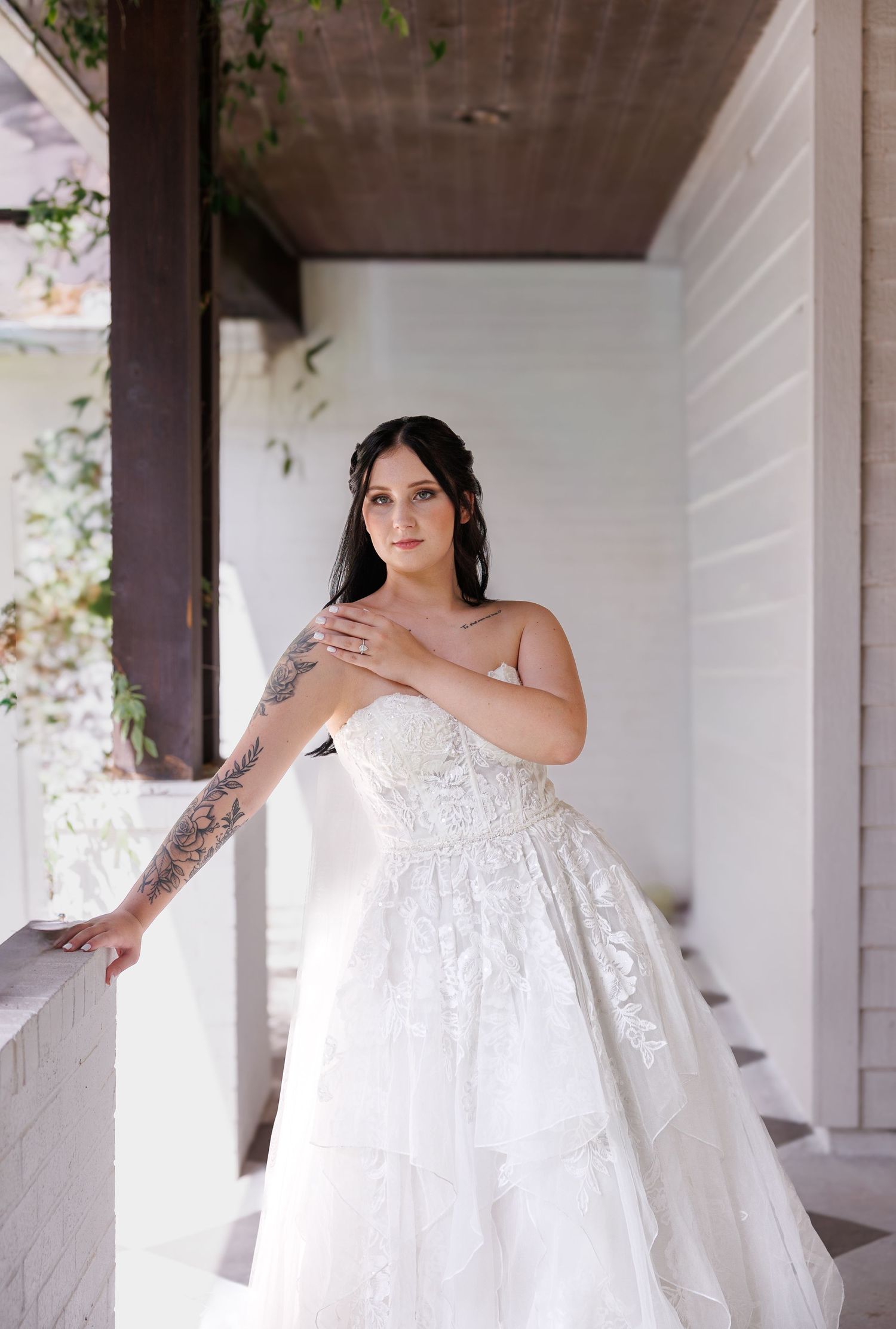 A bride in a flowing white lace gown poses elegantly on a white porch in a series of romantic portraits.