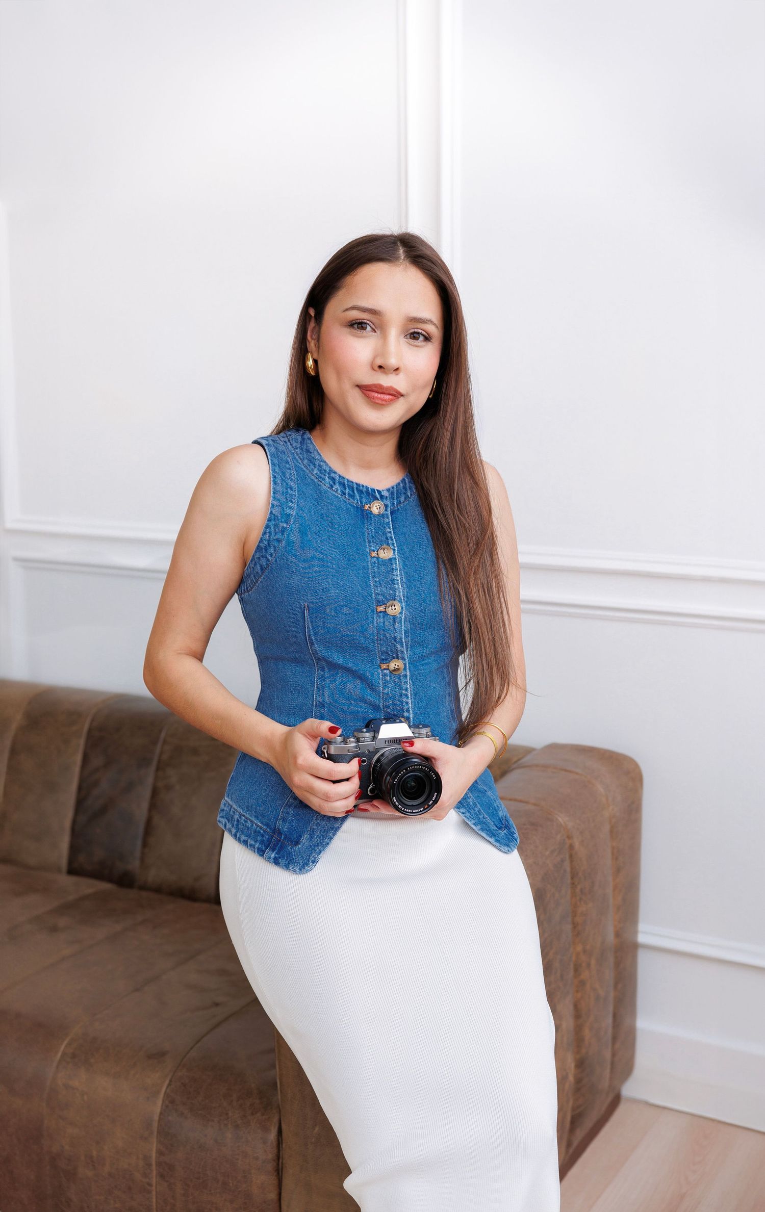 Stylish outfit featuring denim vest and white pencil skirt while posing with camera against white wall.