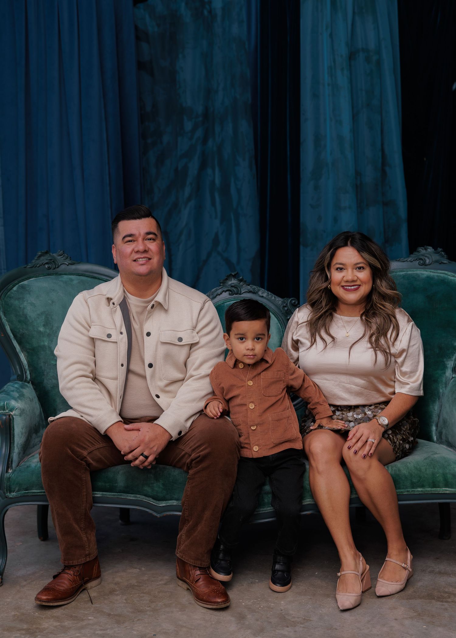 Family wearing matching beige outfits sits together on a bench for a casual outdoor portrait session.