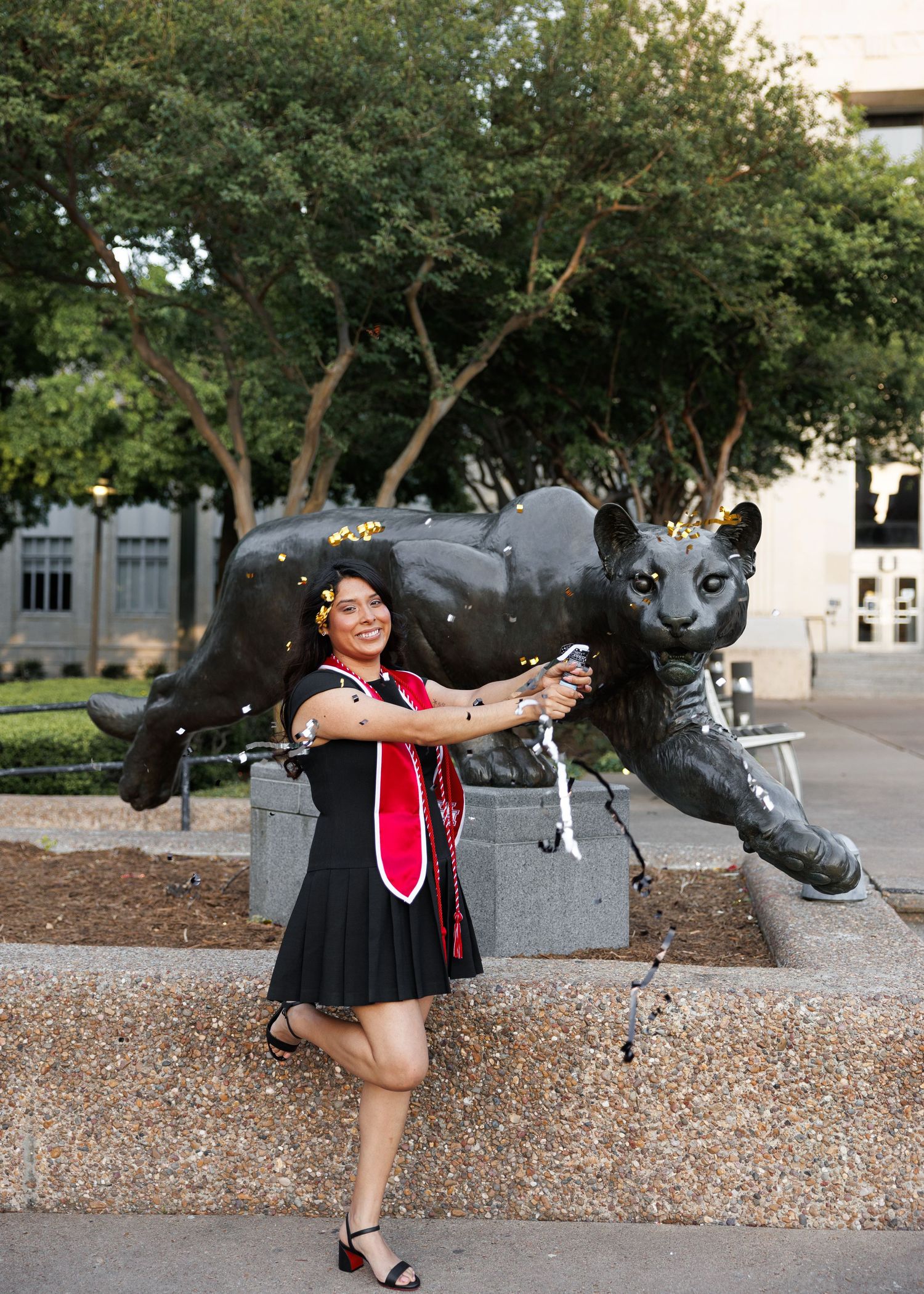 Graduate poses with a large panther mascot statue on a university campus during graduation photo session.