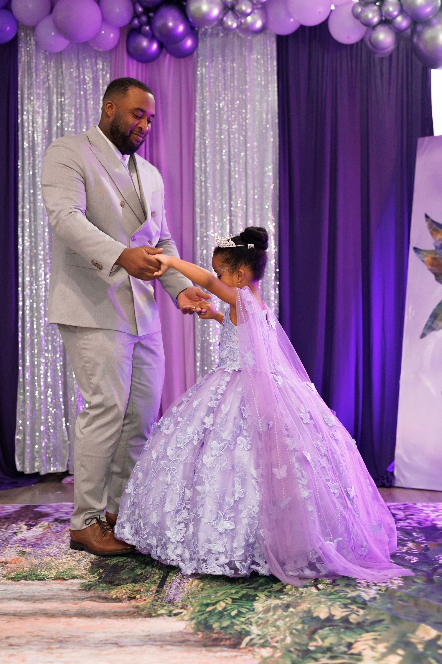 An elegant dance celebration with purple balloon decor, sparkly curtains, and flowing white gowns at a special event.