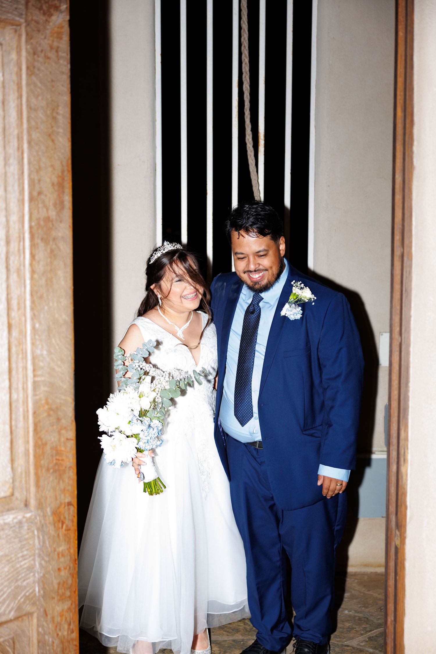 A happy newlywed couple poses together at their wedding ceremony, with the bride in white holding a bouquet.