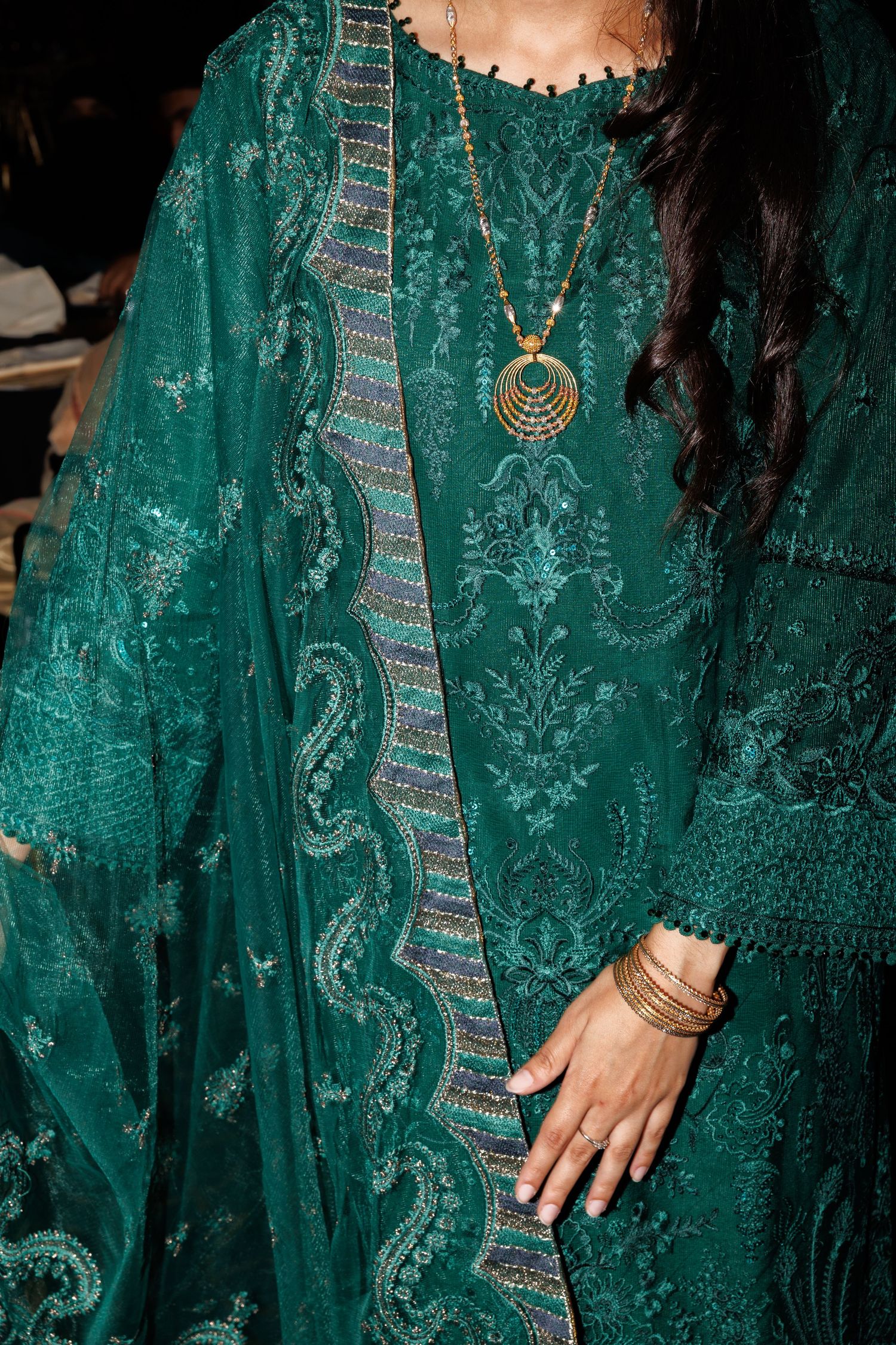 Close-up details of an ornate emerald green lace dress with intricate embroidery and delicate patterns.