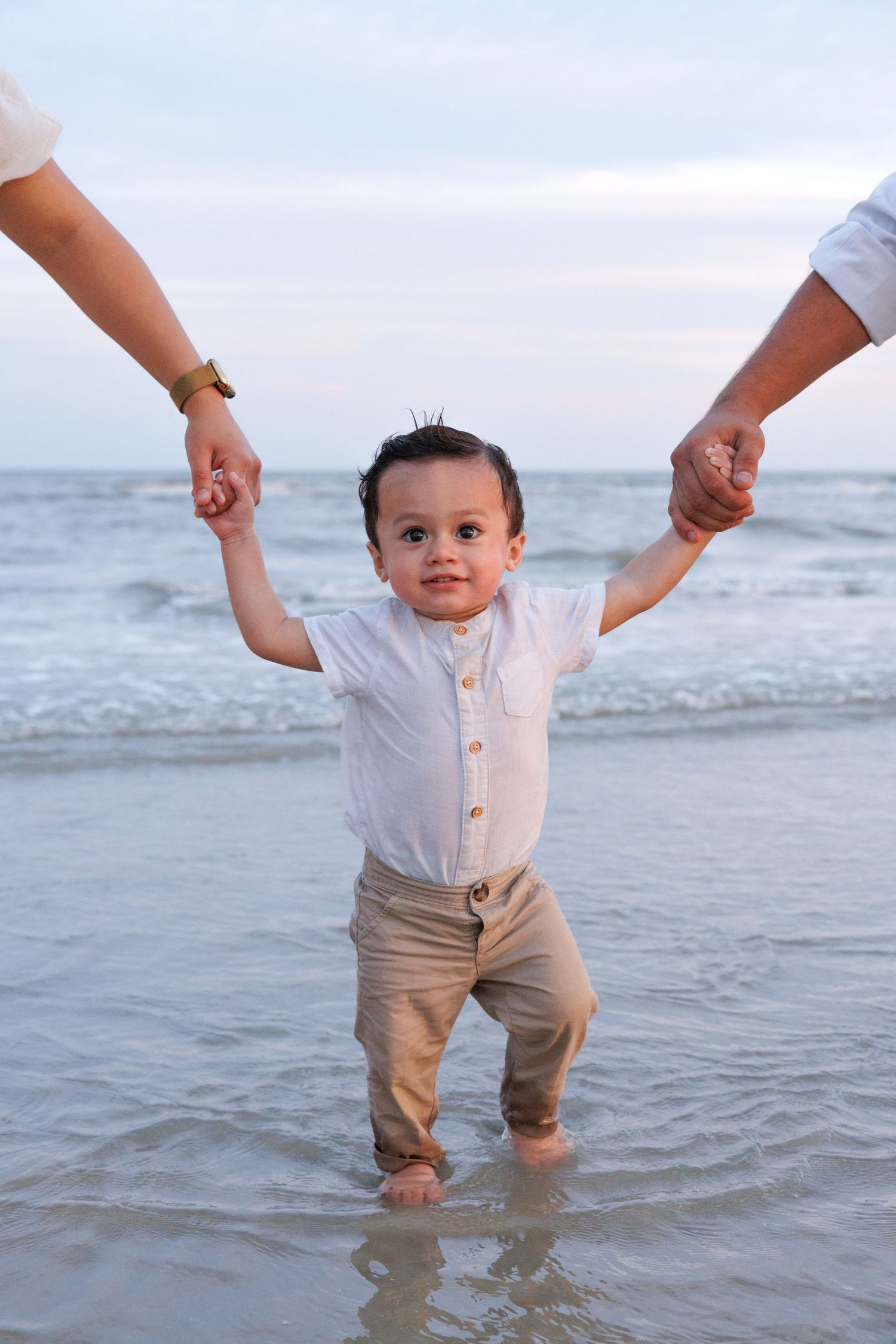 A series of photos showing a small child being held by adult hands while playing in gentle ocean waves at the beach.