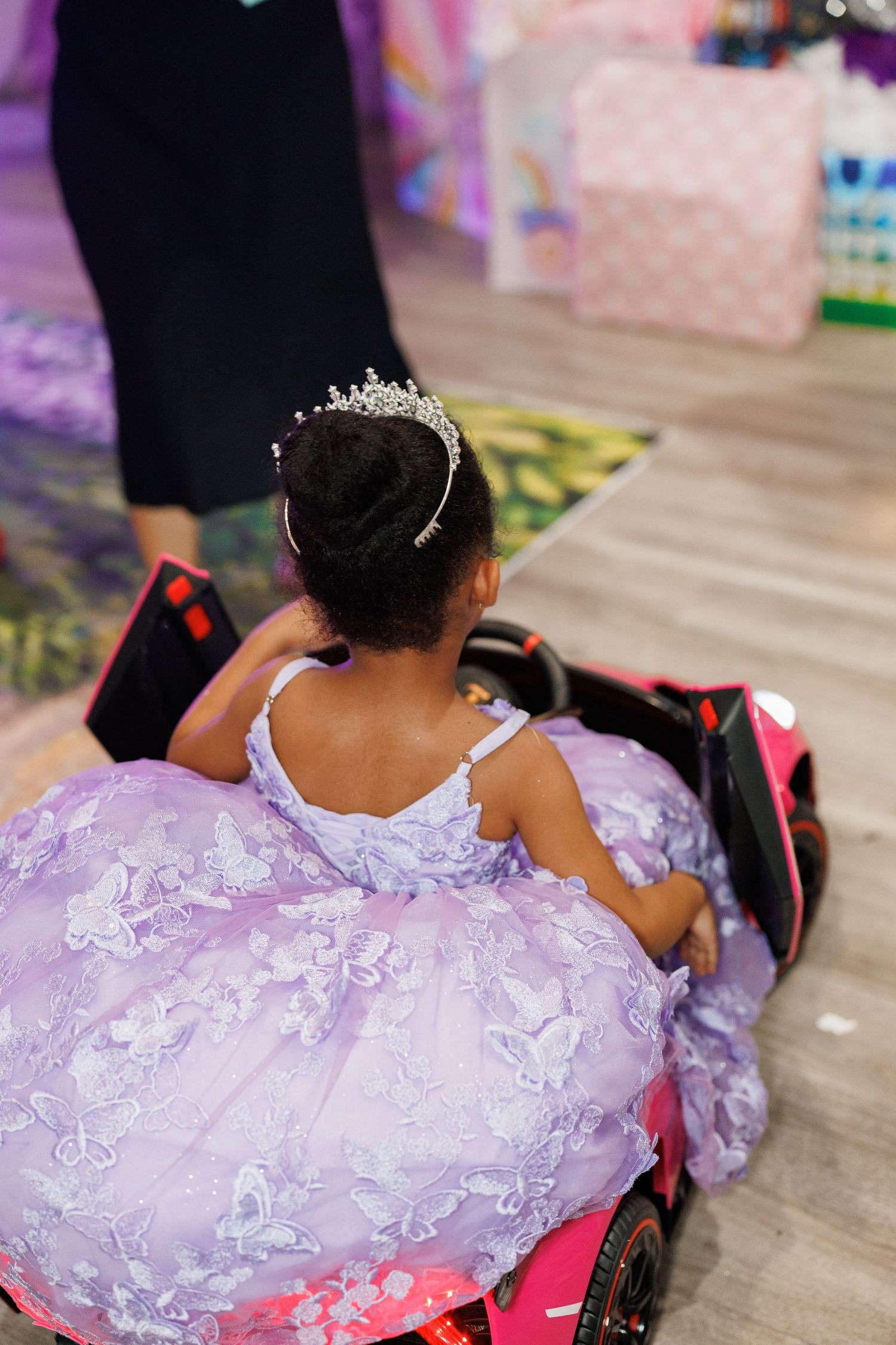 Someone wearing a sparkly purple princess dress and tiara sits in a wheelchair at an event.