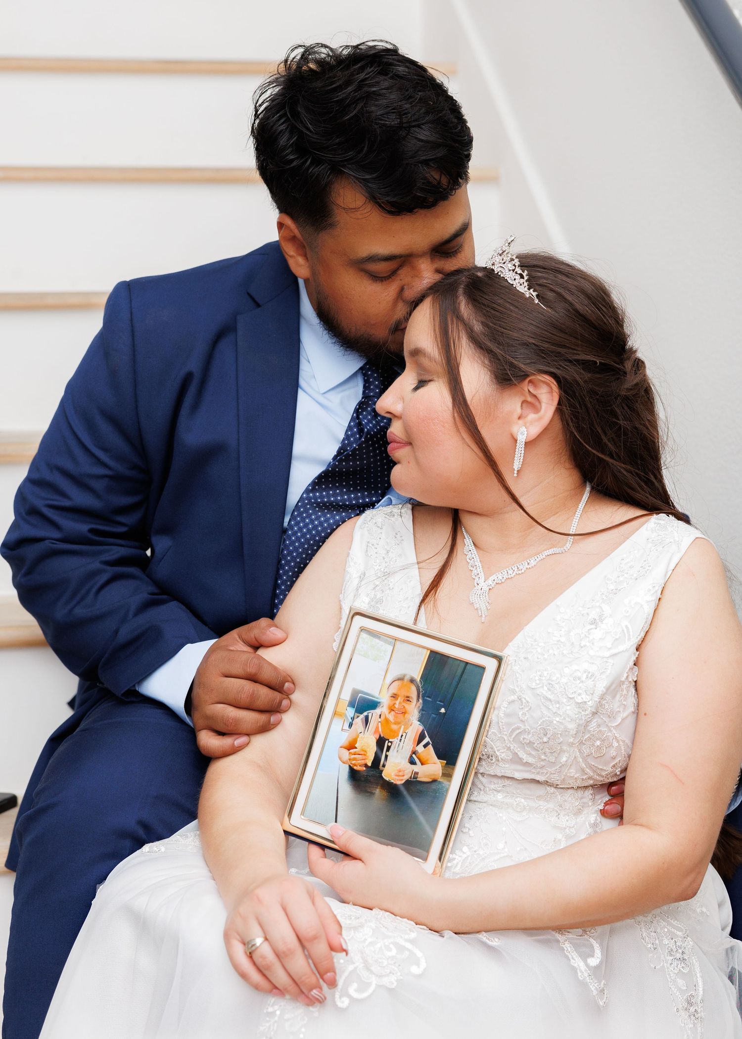 Newlywed couple in navy suit and white dress share intimate moments while holding picture frames during wedding photos.