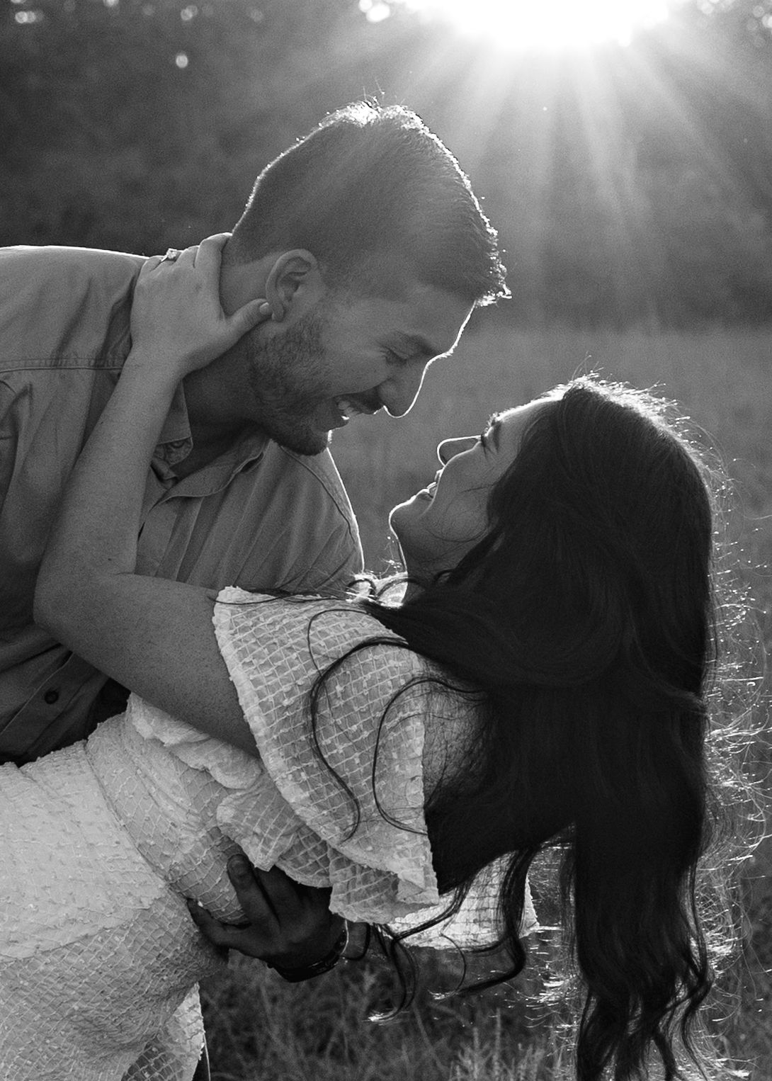 Black and white photo of a couple sharing a romantic moment outdoors, with sunlight streaming behind them.