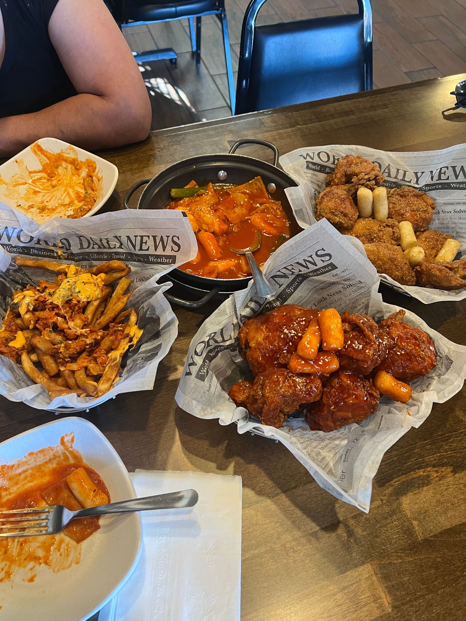 Korean fried chicken and other dishes served on newspaper-style paper at a casual restaurant.