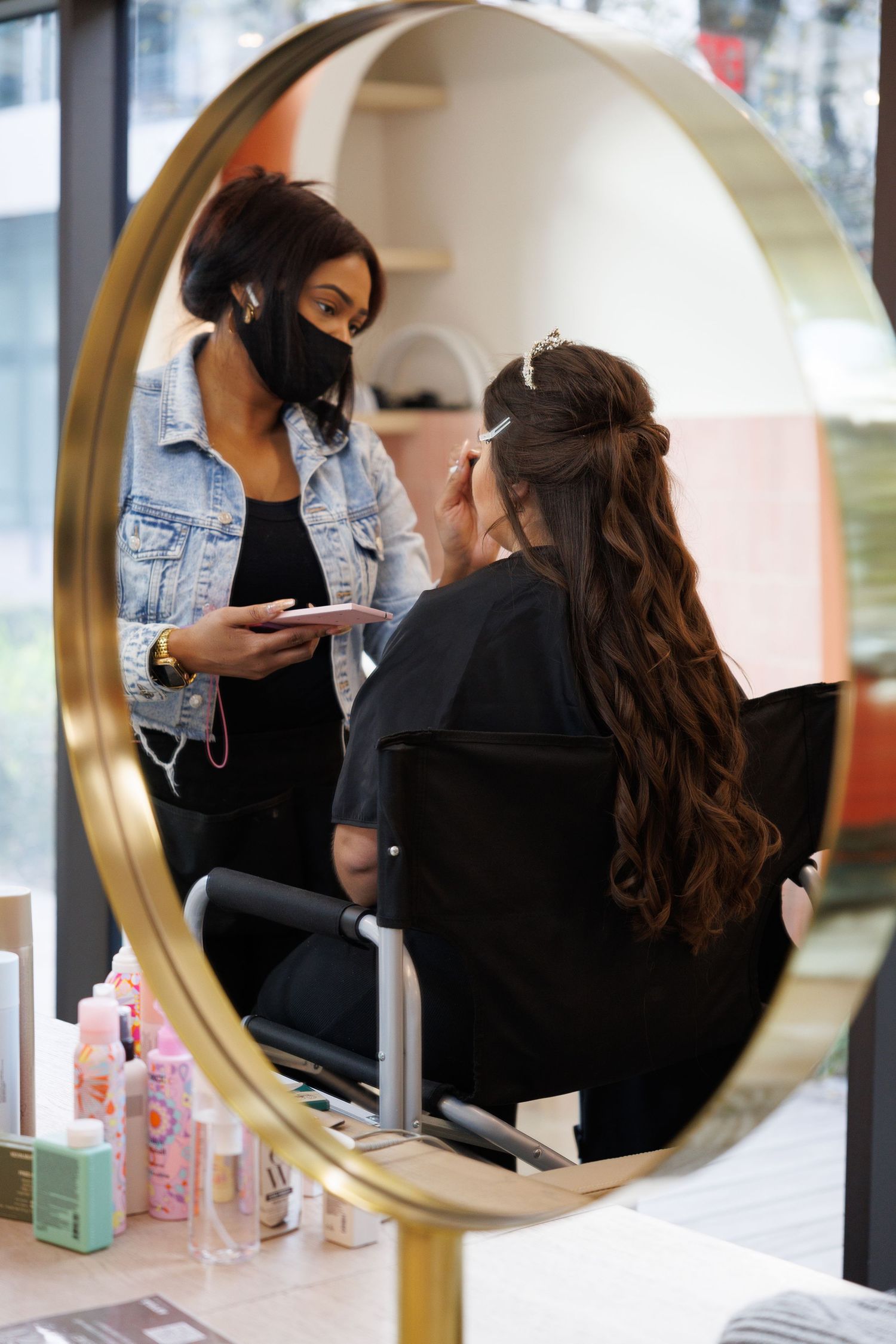 Three connected mirror reflections show a stylist working on a client's hair at a beauty salon.