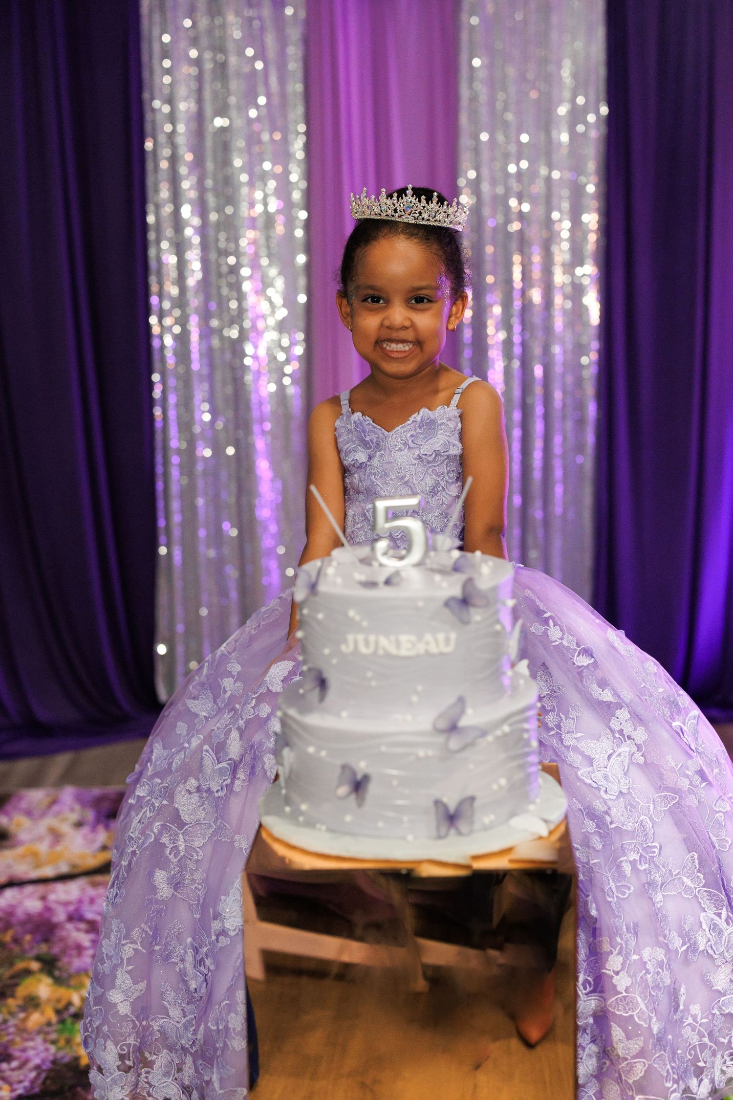 A beautiful 5th birthday celebration with a silver tiered cake and sparkling purple backdrop with lights.