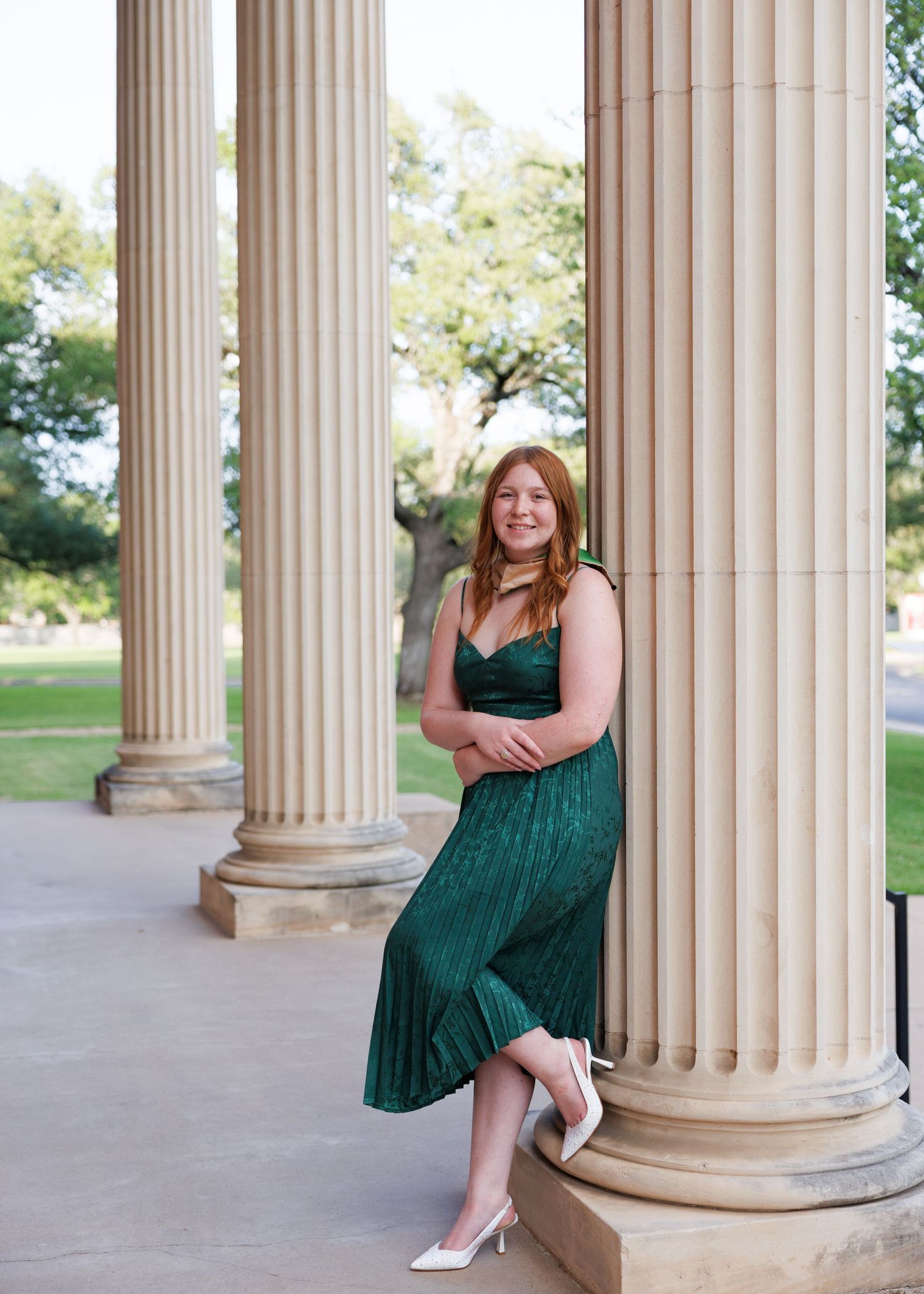 Elegant green velvet dress photographed in series against classical stone columns with outdoor garden backdrop.