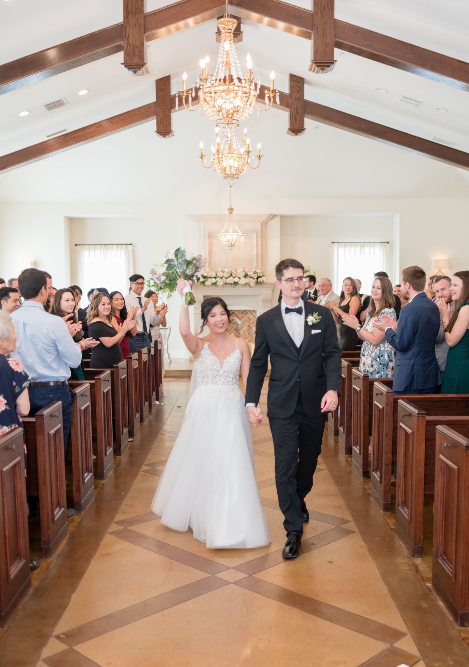 Wedding ceremony in a chapel with wood pews and crystal chandeliers showing a progression from standing to joyful exit.