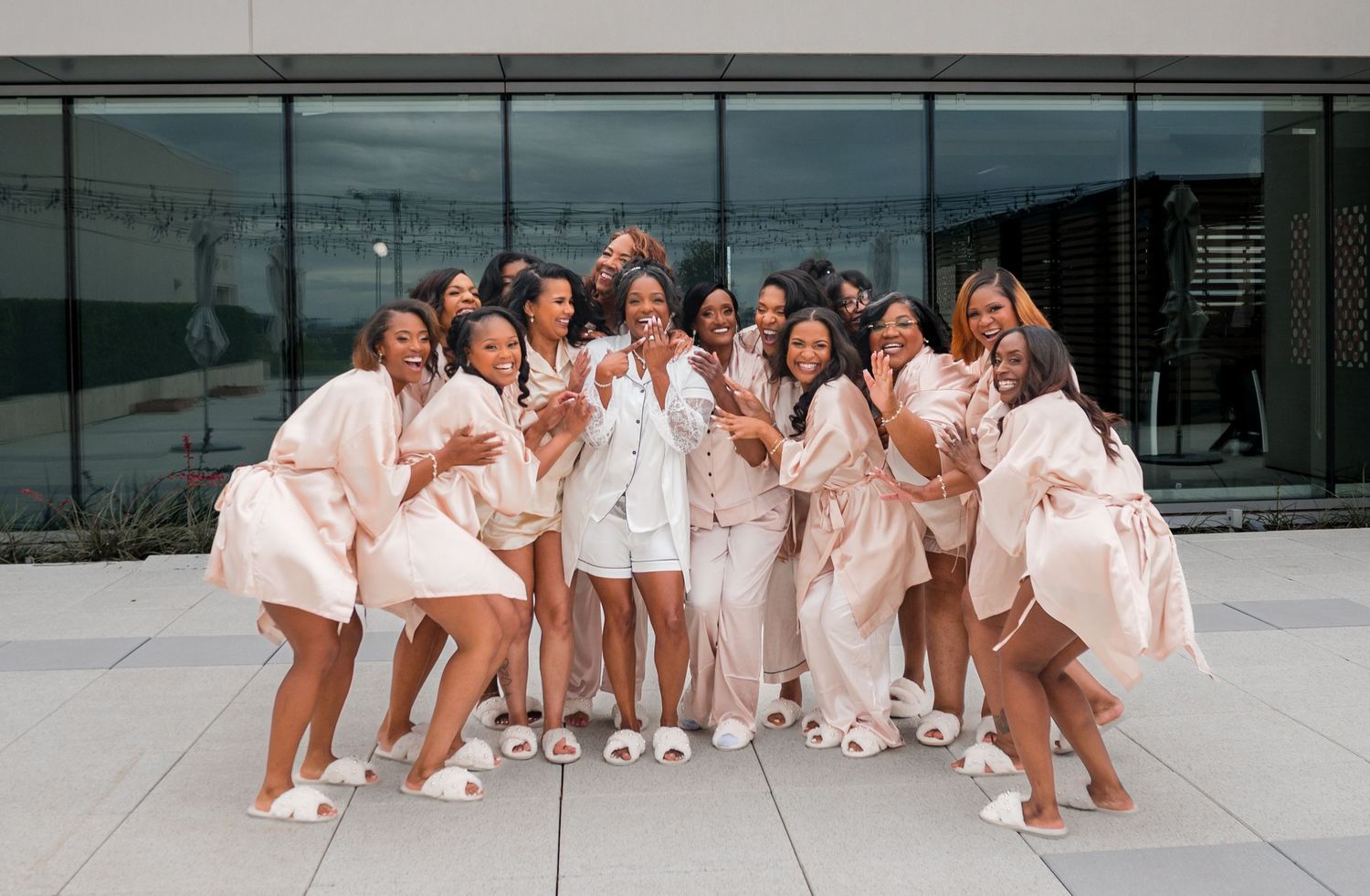 Bridal party in matching blush robes and white slippers posing together outdoors before a wedding celebration.