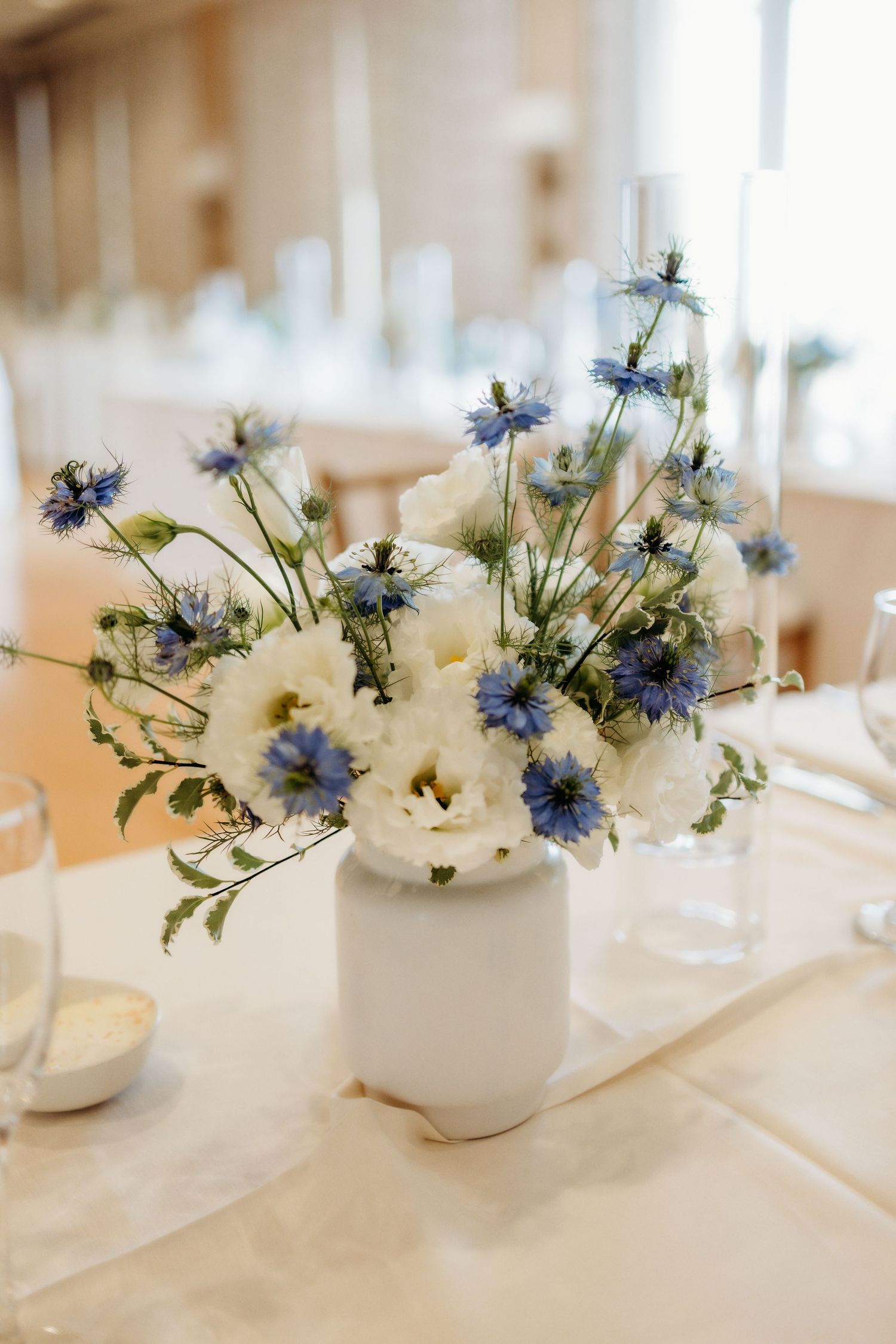 Delicate blue and white floral centerpiece arrangements in small white vases on an elegant table setting.