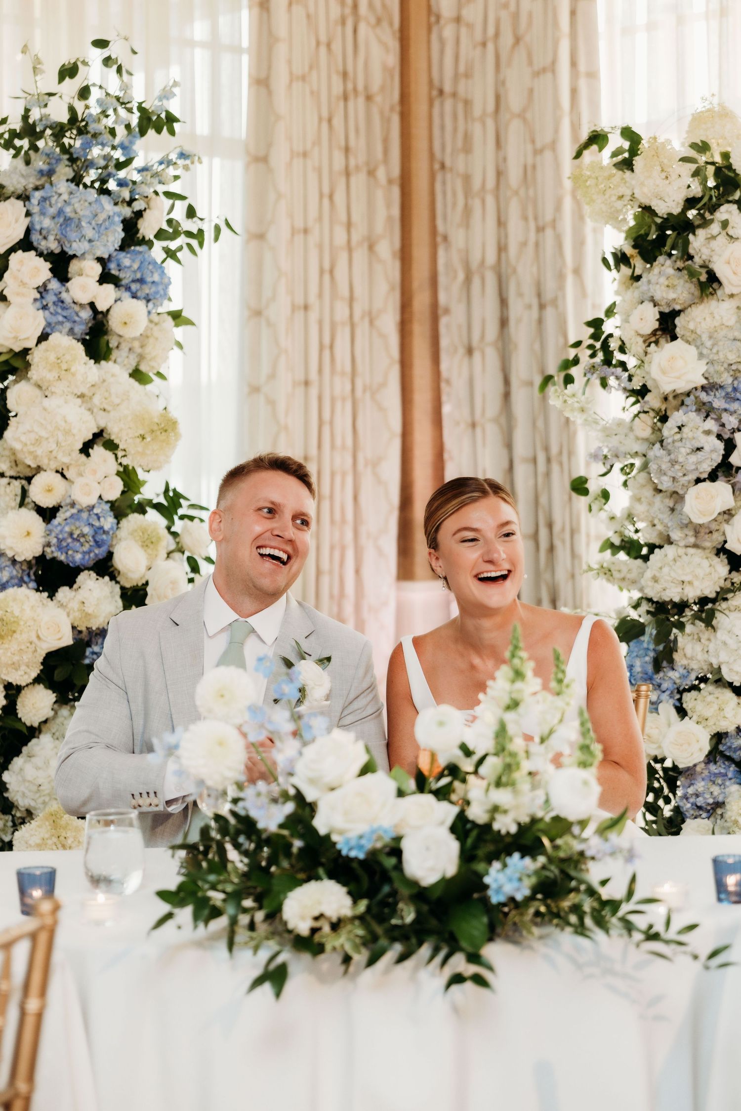 An elegant wedding reception head table decorated with white and blue floral arrangements.