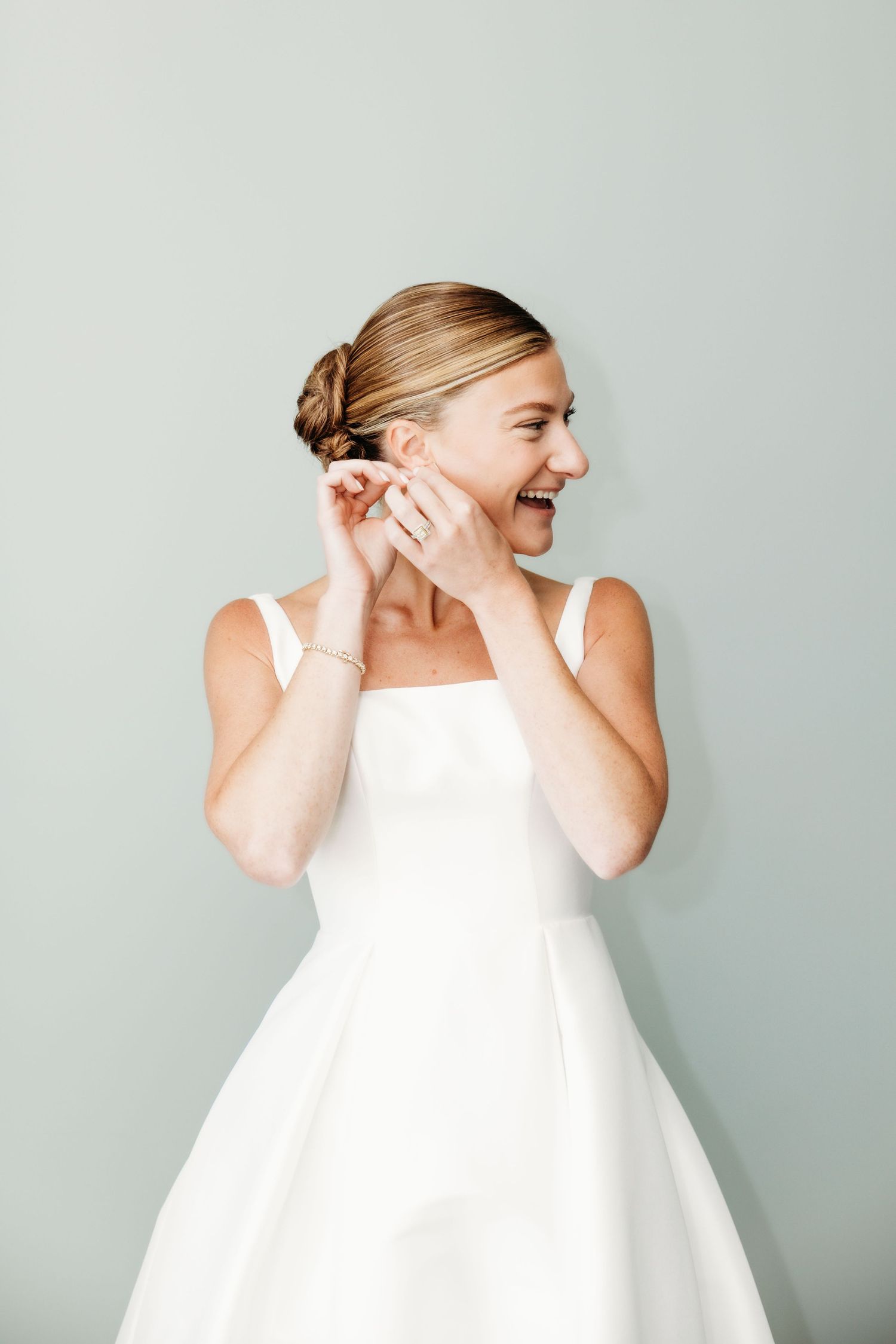 A person in a white dress laughs and gestures expressively in a series of four candid poses against a gray background.