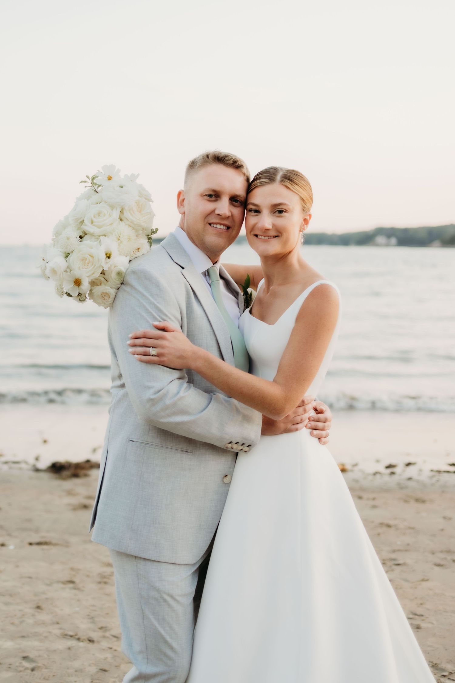 Newlyweds sharing intimate moments on a beach at sunset with white orchid bouquet.