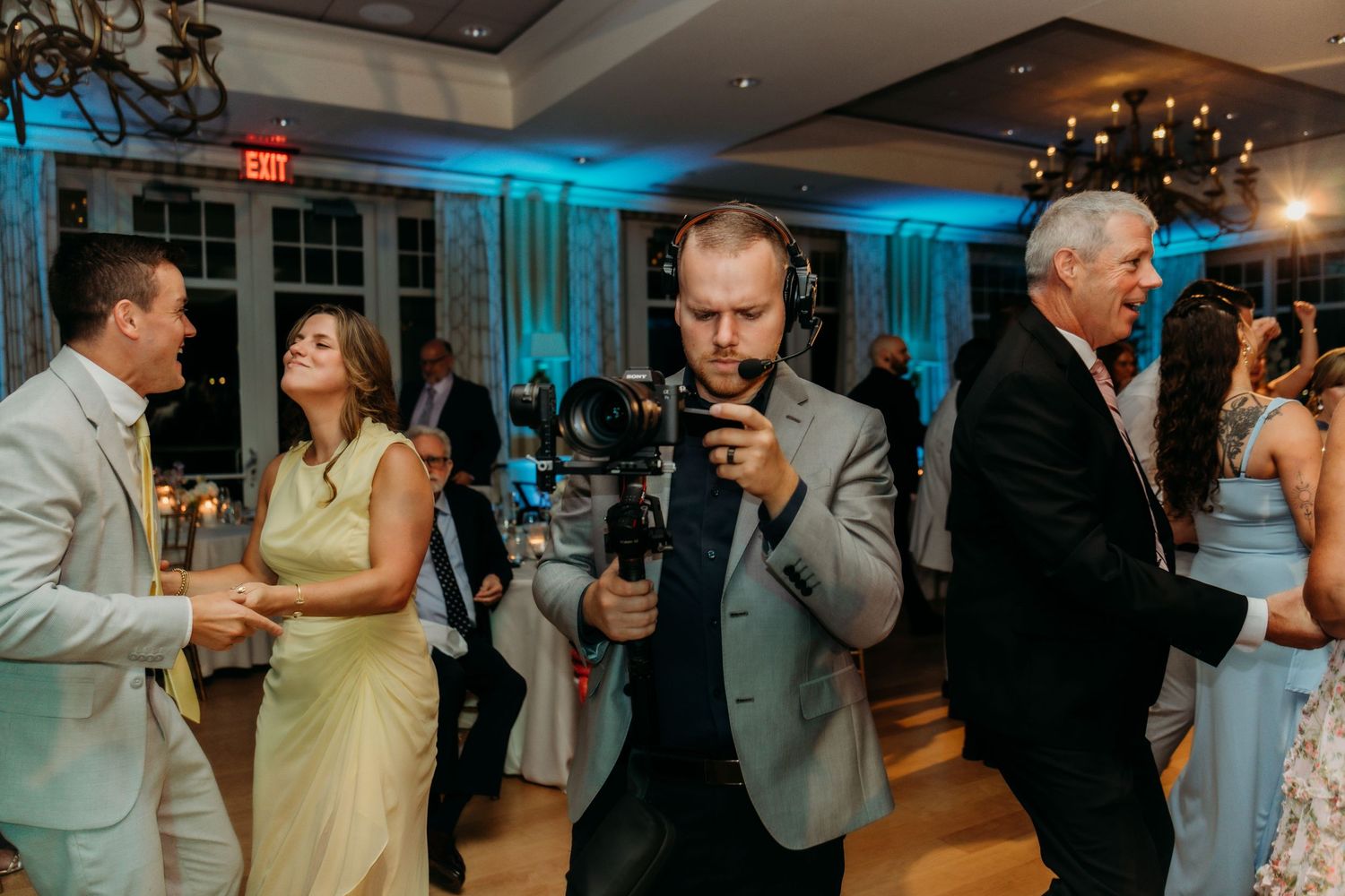 Couples dancing together at an indoor wedding reception with blue mood lighting and elegant decor.