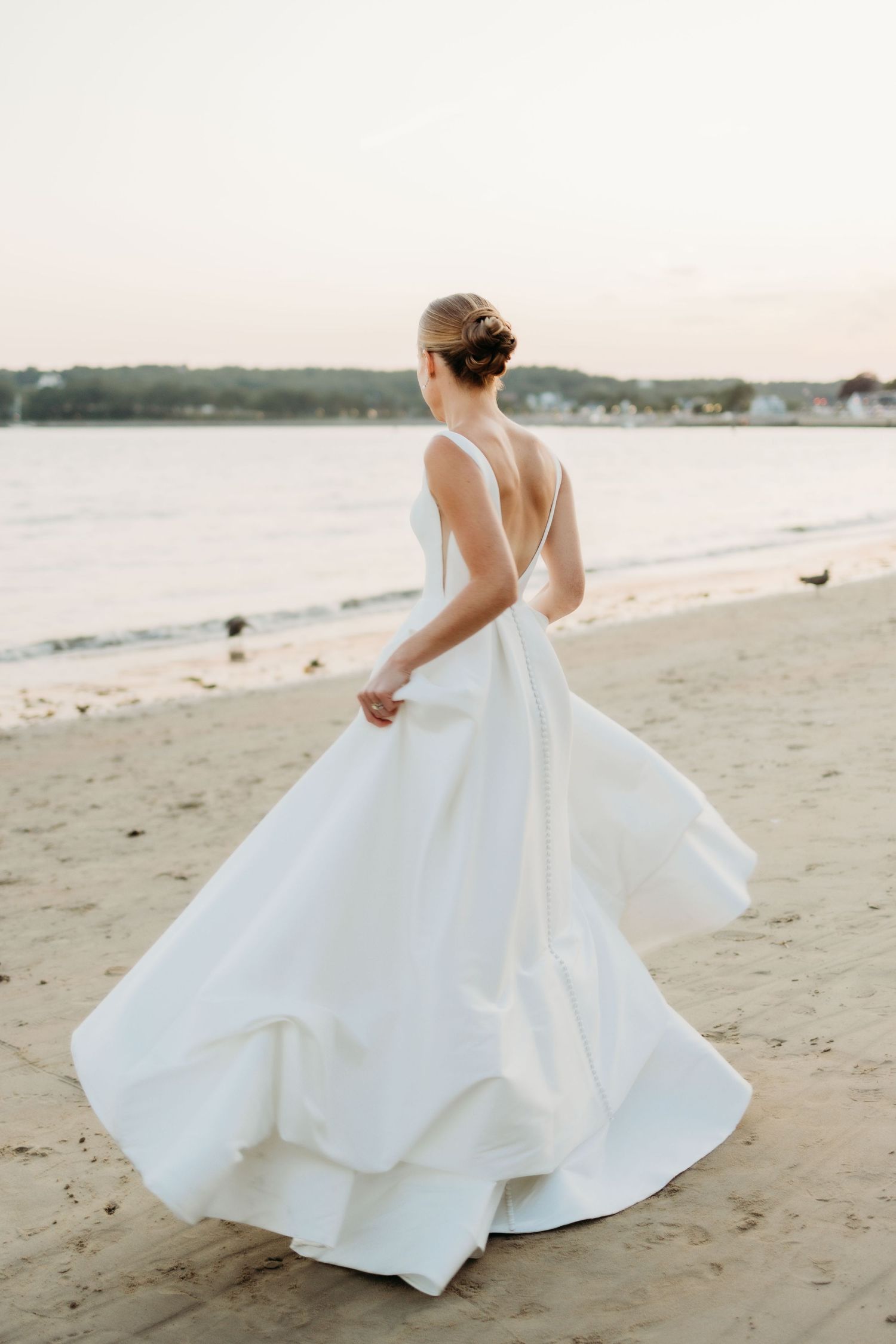 A flowing white wedding dress twirls gracefully on a sandy beach at sunset.