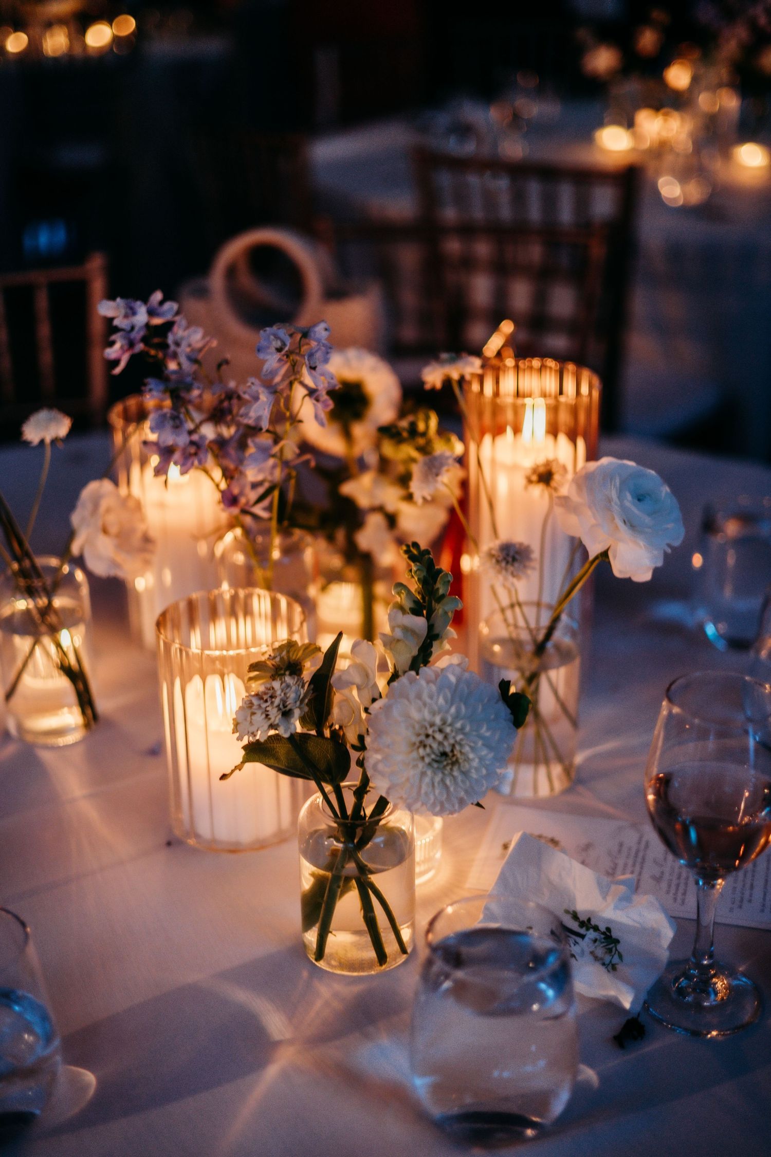 Romantic candlelit wedding reception table with delicate floral centerpieces in glass vases.