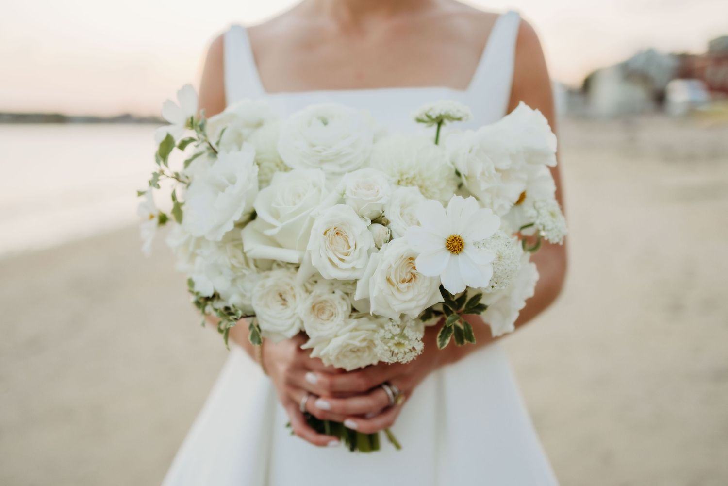 Close-up of white rose and daisy wedding bouquets against a light background.