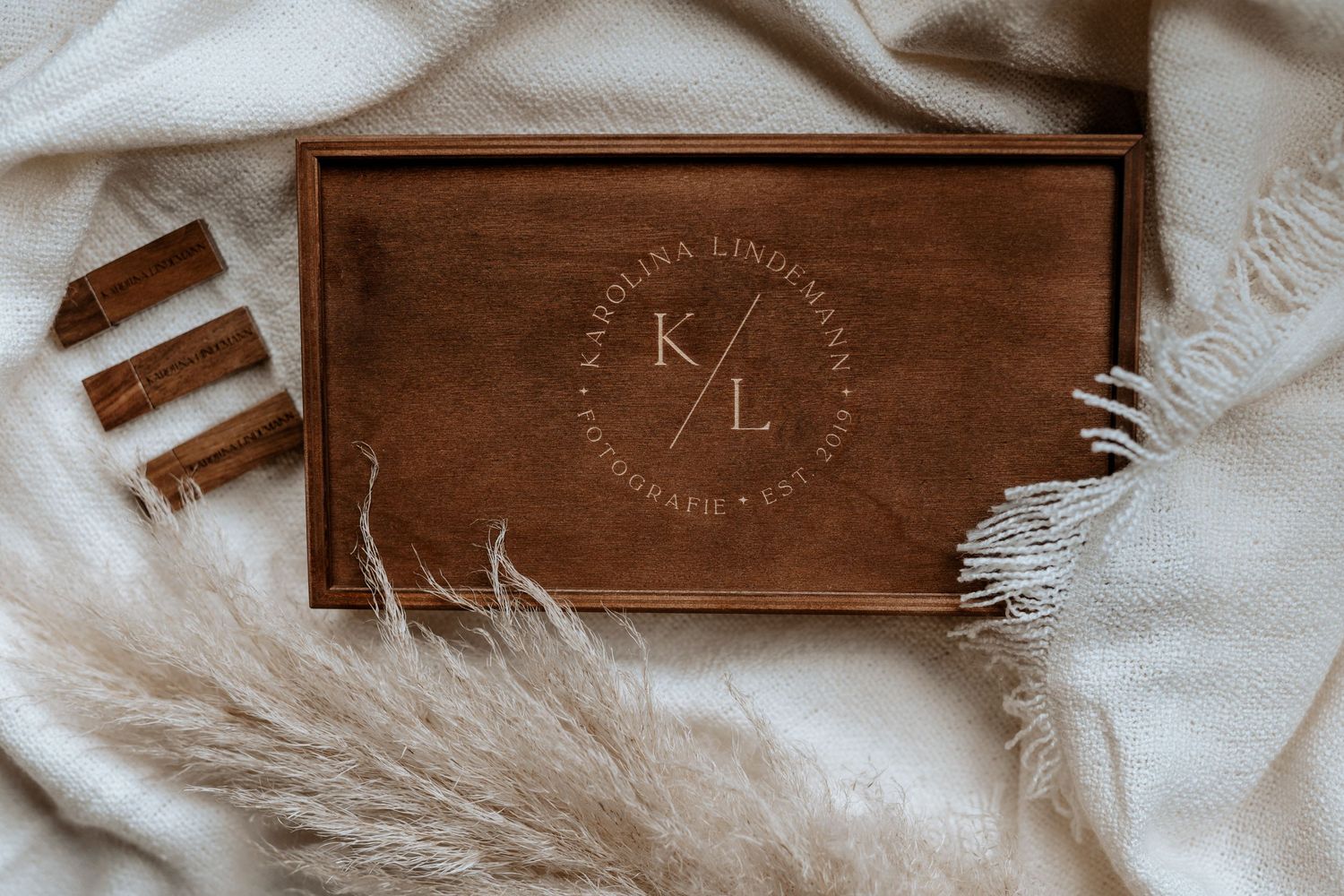 Wooden box with monogram logo on fabric background with pampas grass.