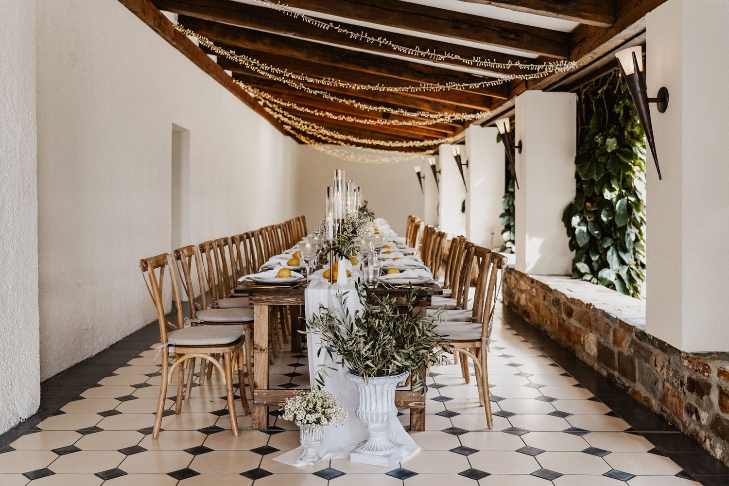An elegant wedding reception table setup with rustic decor and string lights in a white corridor.