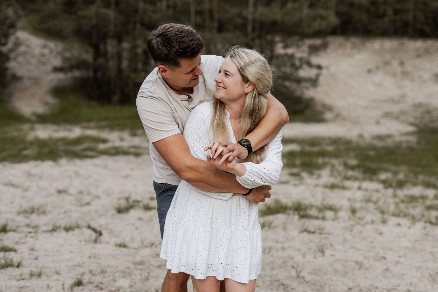 Couple in white outfits shares romantic moments together on a sandy beach during sunset.