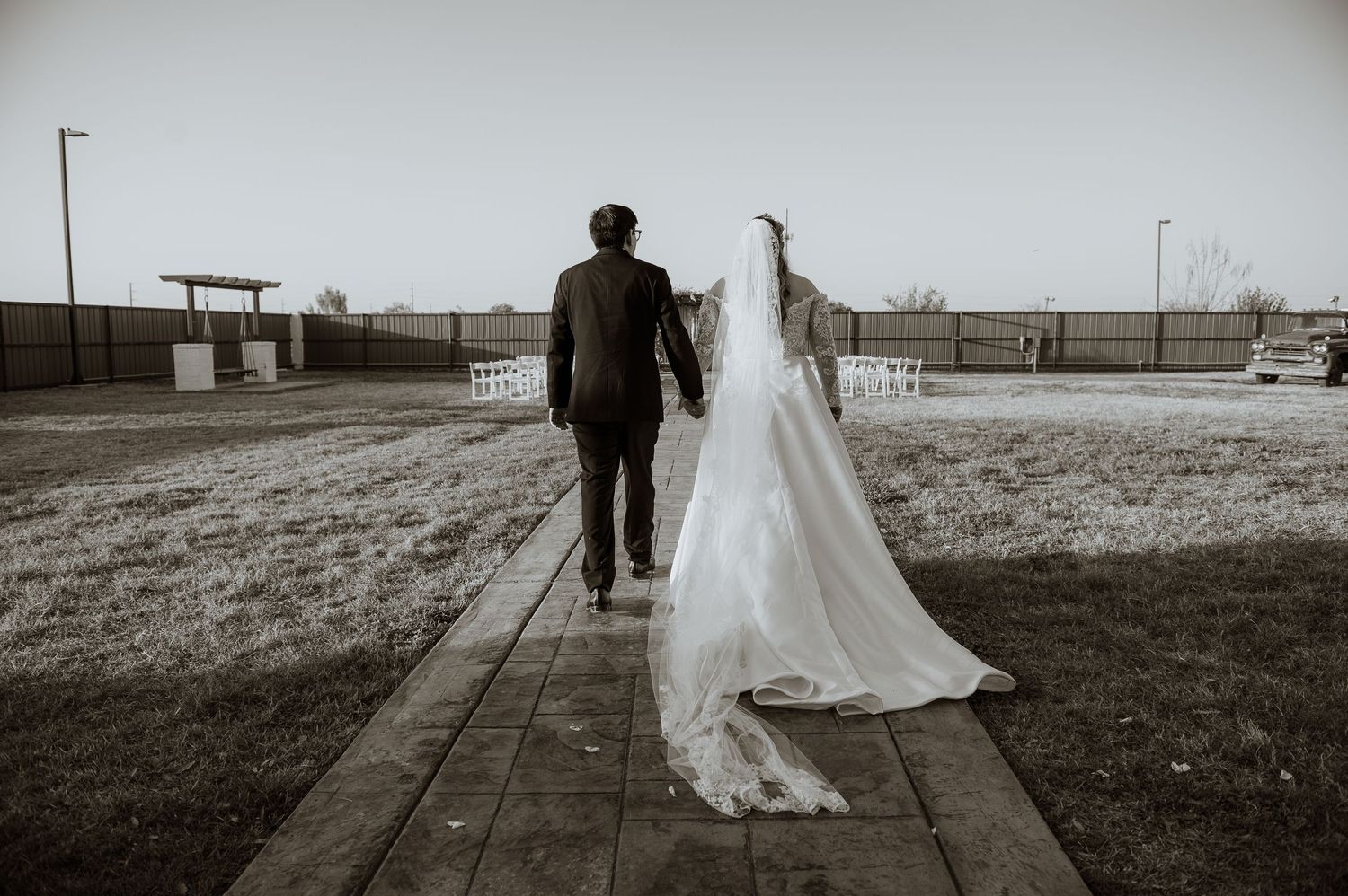 A bride and groom walk hand-in-hand down a brick path in a sepia-toned outdoor wedding photo.